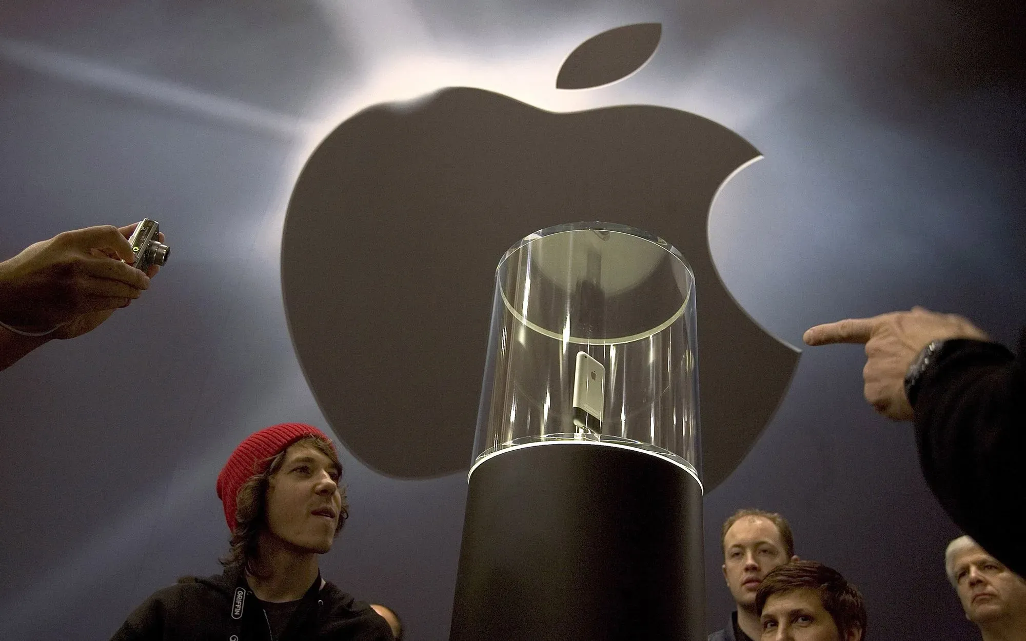 جمهور يتفاعل مع عرض أول هاتف آيفون في حدث من Apple، مع شعار الشركة خلفهم، مما يعكس أهمية الابتكار في عالم التكنولوجيا.