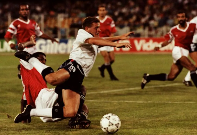 لاعب إنجليزي يتعرض لتدخل دفاعي قوي من لاعب منتخب مصر خلال مباراة في كأس العالم 1990، تعكس قوة المنافسة والتكتيك الدفاعي في البطولة.