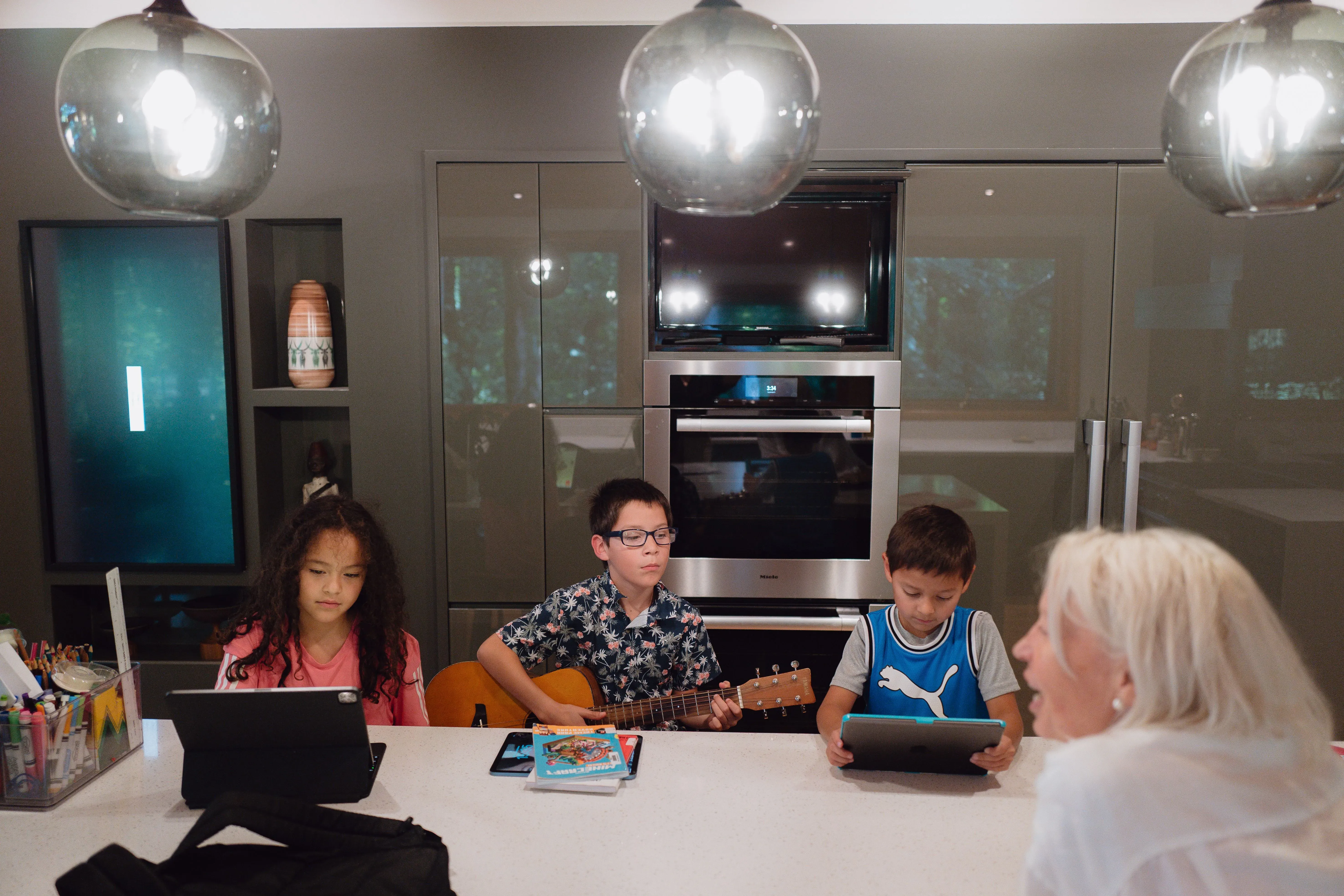 فيبي وأنجيلو، طفلان أمريكيان، يجلسان مع أطفال آخرين في مطبخ حديث، يعبرون عن الحزن بسبب فقدان والدتهما بسبب إجراءات الهجرة.