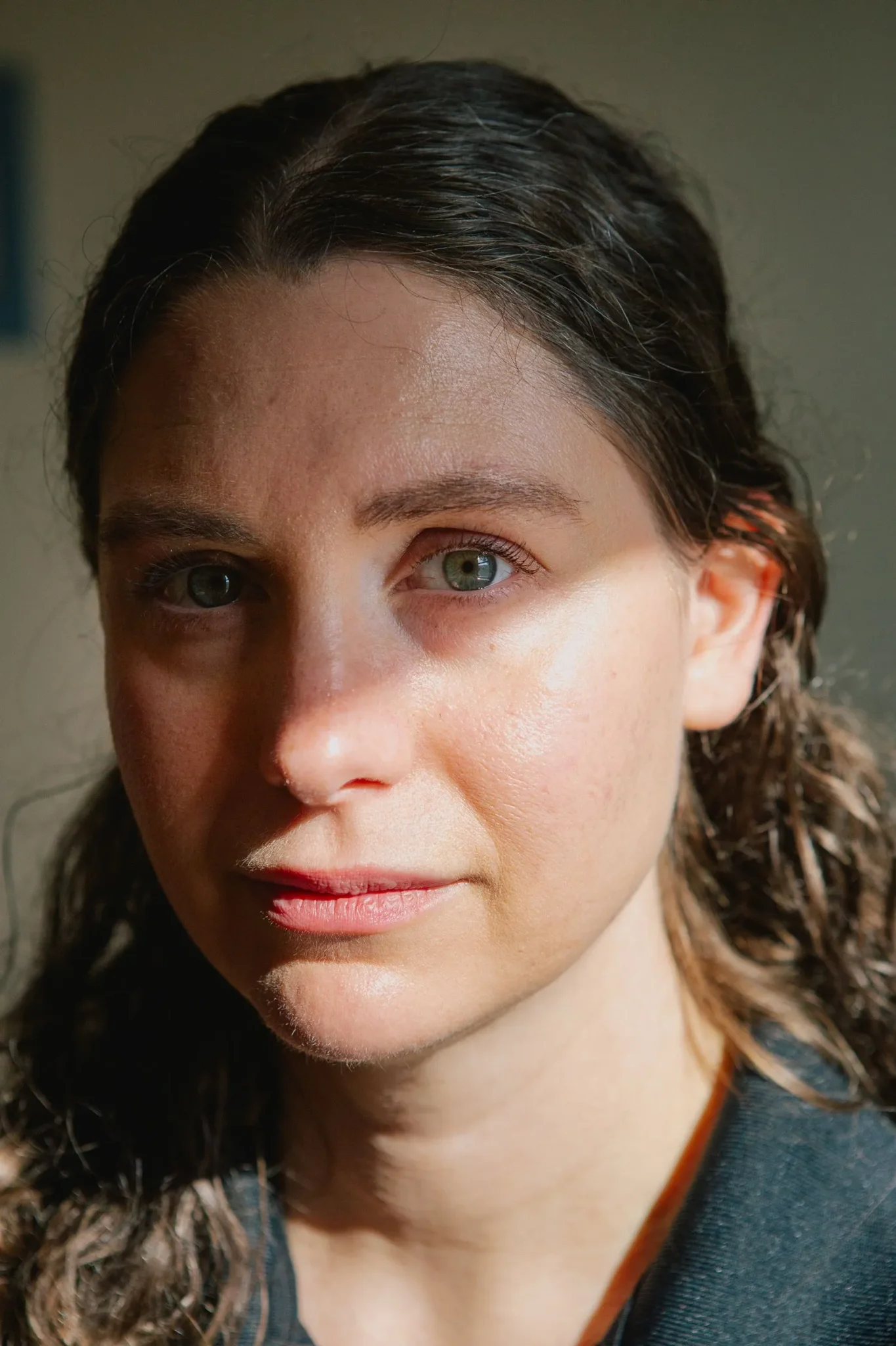 امرأة شابة ذات شعر بني طويل وعيون خضراء تنظر بجدية، تعكس صورة طبيبة تعالج تفشي الحصبة في بنسلفانيا.