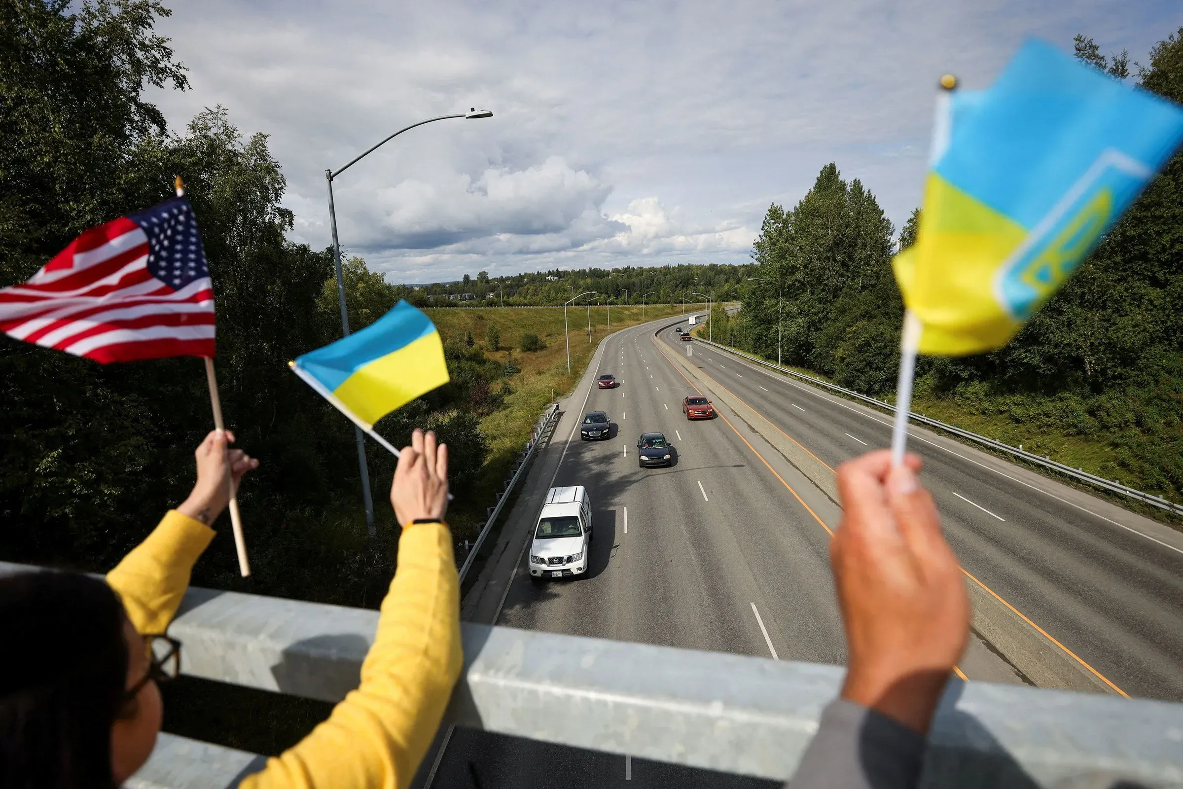 أشخاص يحملون أعلام أوكرانية وأمريكية على جسر يطل على طريق مزدحم، يعبرون عن دعمهم للأوكرانيين في الولايات المتحدة.