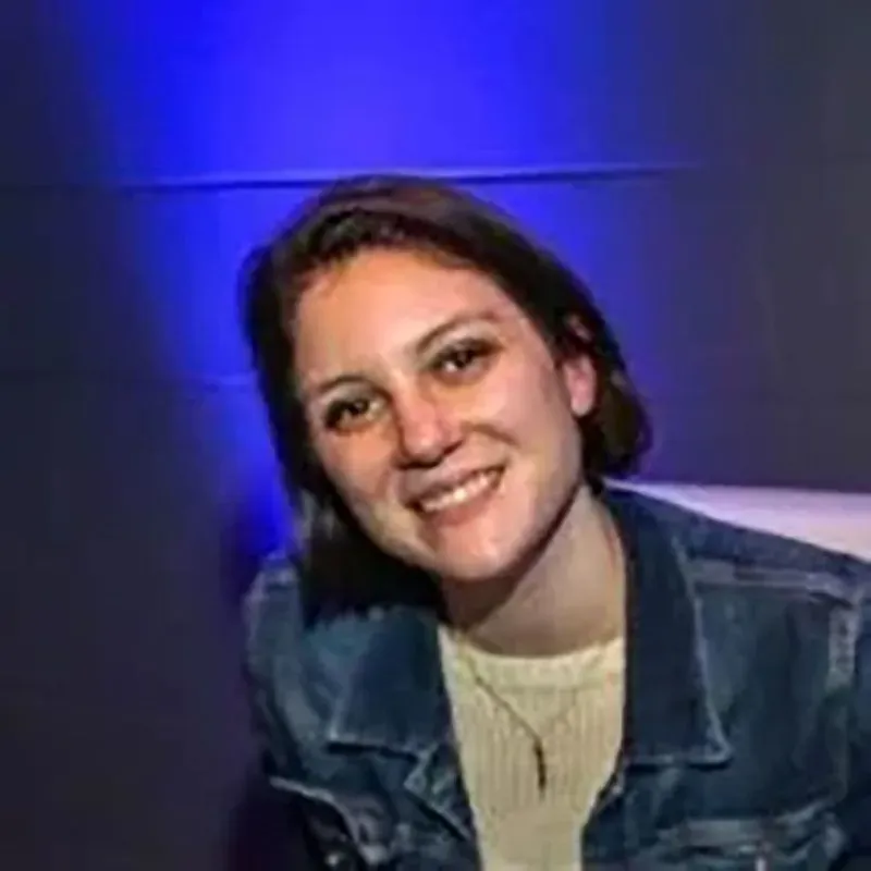 صورة لامرأة مبتسمة ترتدي سترة جينز، تظهر في خلفية مضاءة بألوان زرقاء، تعكس أجواء مريحة.