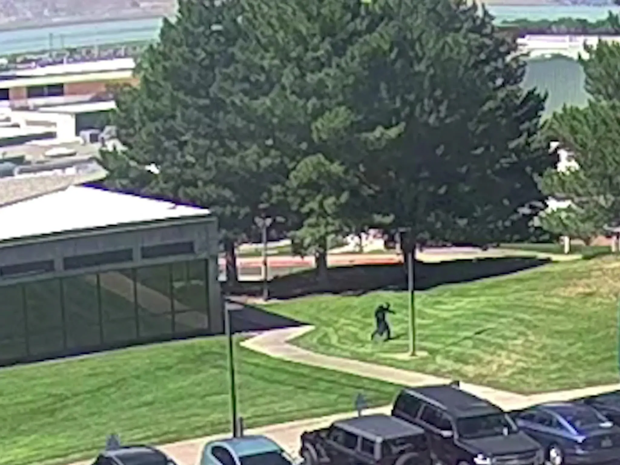 شخص يرتدي ملابس داكنة يجري في منطقة مشجرة بالقرب من مبنى جامعي، بعد حادث إطلاق نار استهدف ناشطًا سياسيًا في يوتا.