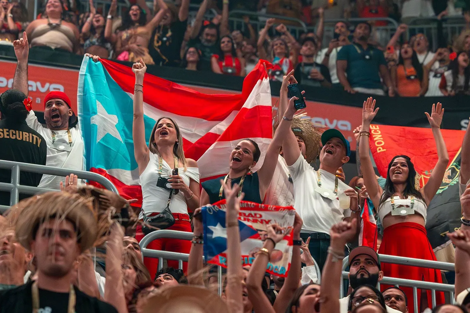 جمهور متحمس في حفل باد باني، يحملون الأعلام البورتوريكية ويرتدون ملابس ملونة، يعبرون عن الفخر الوطني والتضامن خلال الذكرى السنوية لإعصار ماريا.