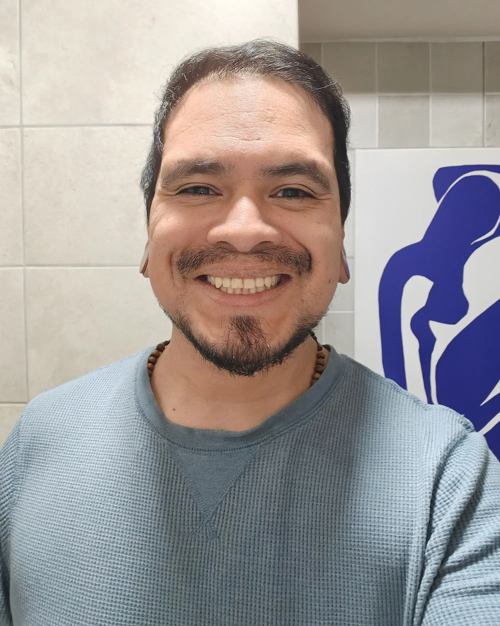 ابتسامة رجل يرتدي سترة زرقاء، يظهر بفروة رأس ناعمة، تعكس شعور الارتياح بعد حلاقة شعره، في حمام منزله.