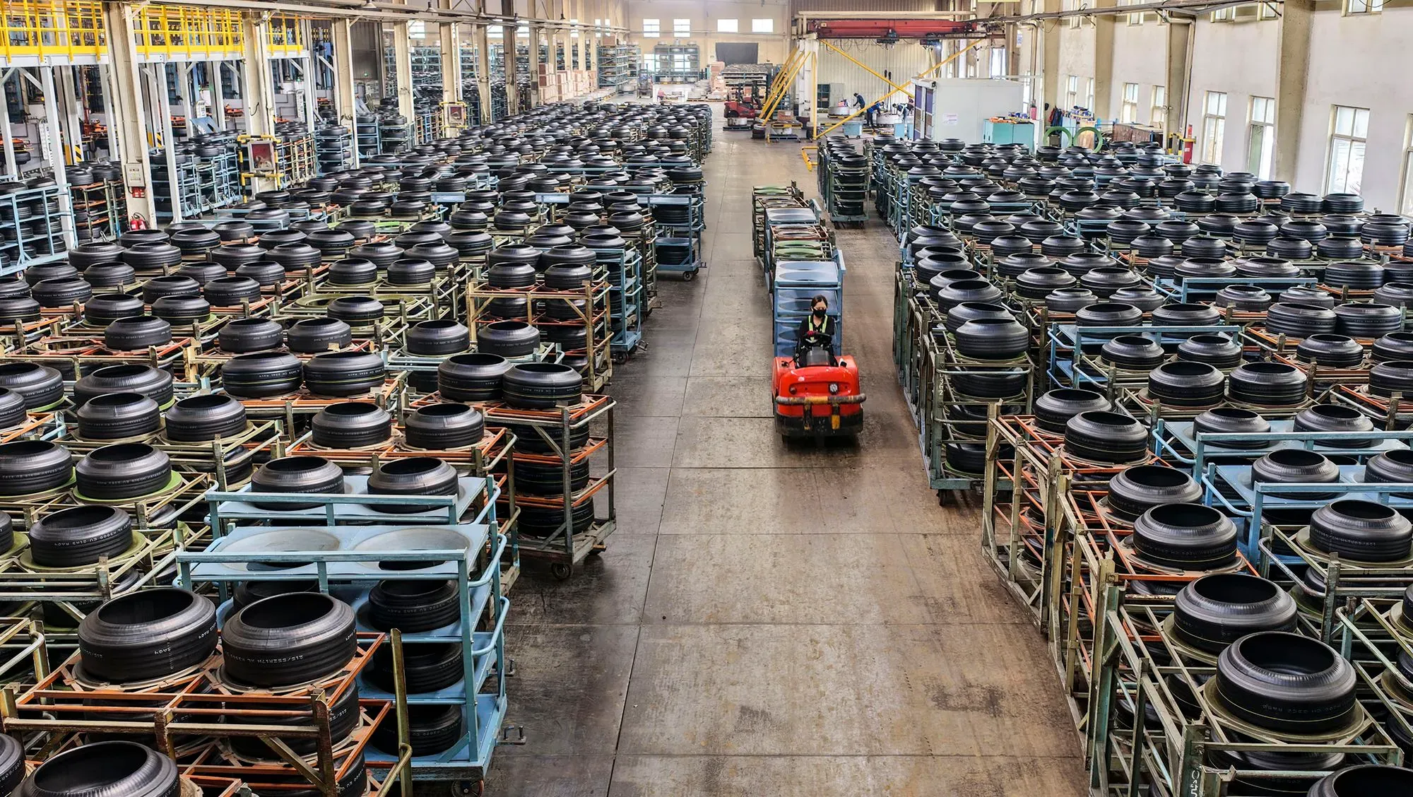 مستودع يحتوي على صفوف من الإطارات السوداء المكدسة على رفوف، مع وجود شاحنة صغيرة تسير بين الممرات، مما يعكس نشاط الصناعة.