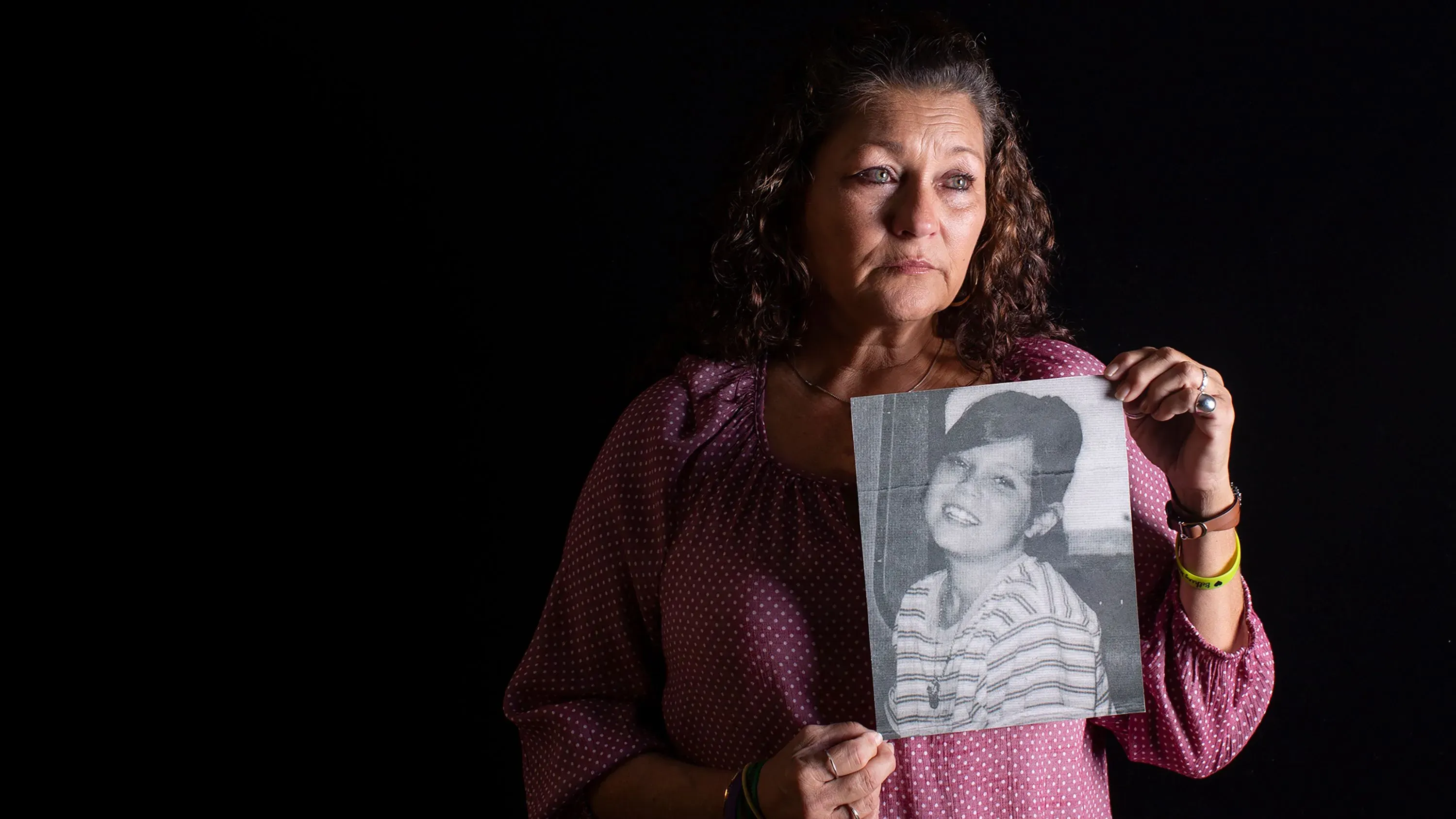 امرأة تحمل صورة قديمة لابنتها المفقودة، تعبر عن مشاعر الحزن والألم في ذكرى اختفائها.