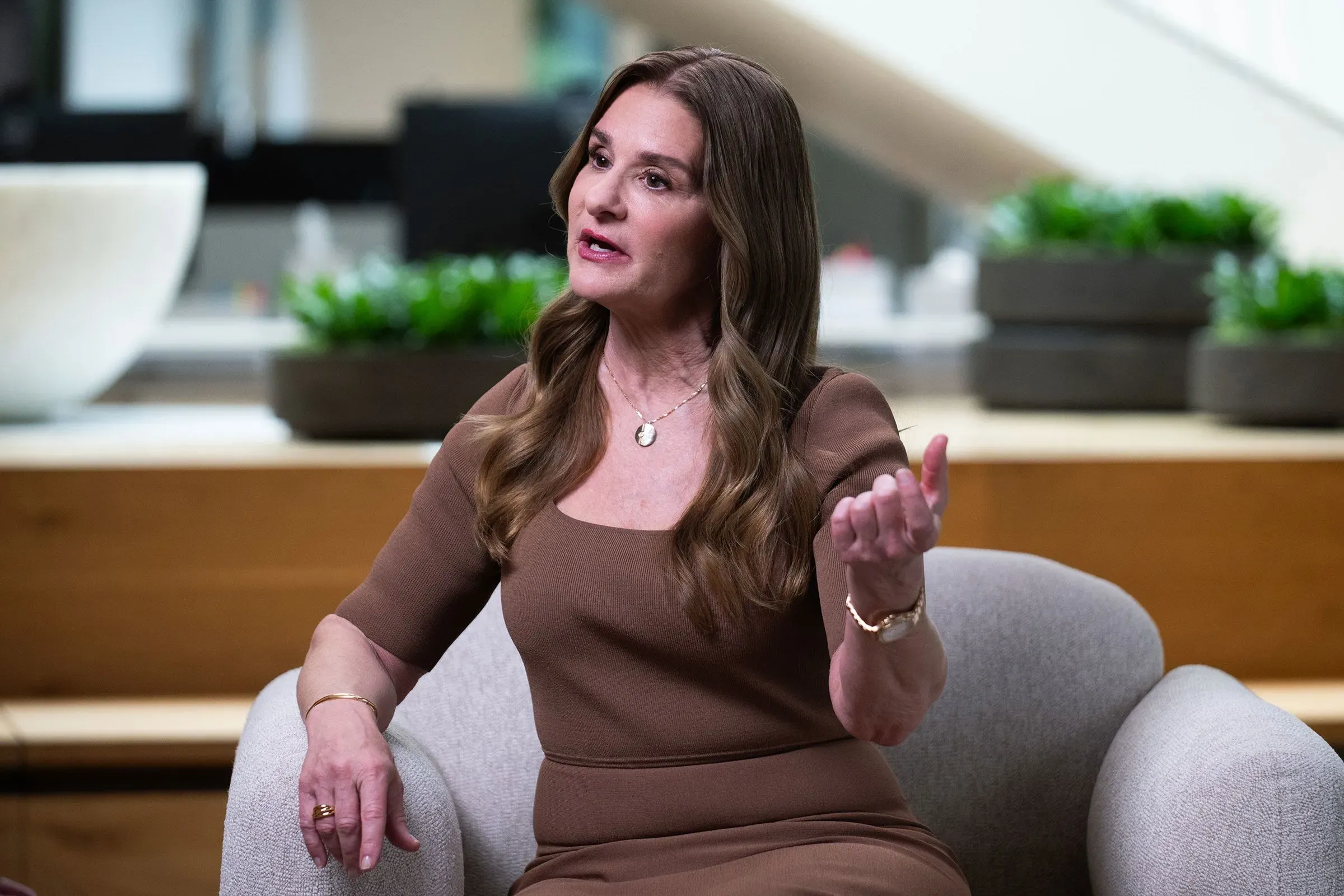 امرأة تتحدث بجدية أثناء جلوسها على أريكة، محاطة بنباتات خضراء، في سياق مناقشة حول العلاقات الخيرية لبيل غيتس.