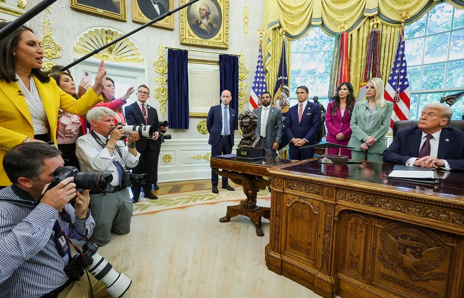 اجتماع في المكتب البيضاوي حيث تظهر مجموعة من الأشخاص بينهم دونالد ترامب، مع صحفيين يلتقطون الصور، مما يعكس التوتر السياسي حول حرية التعبير.
