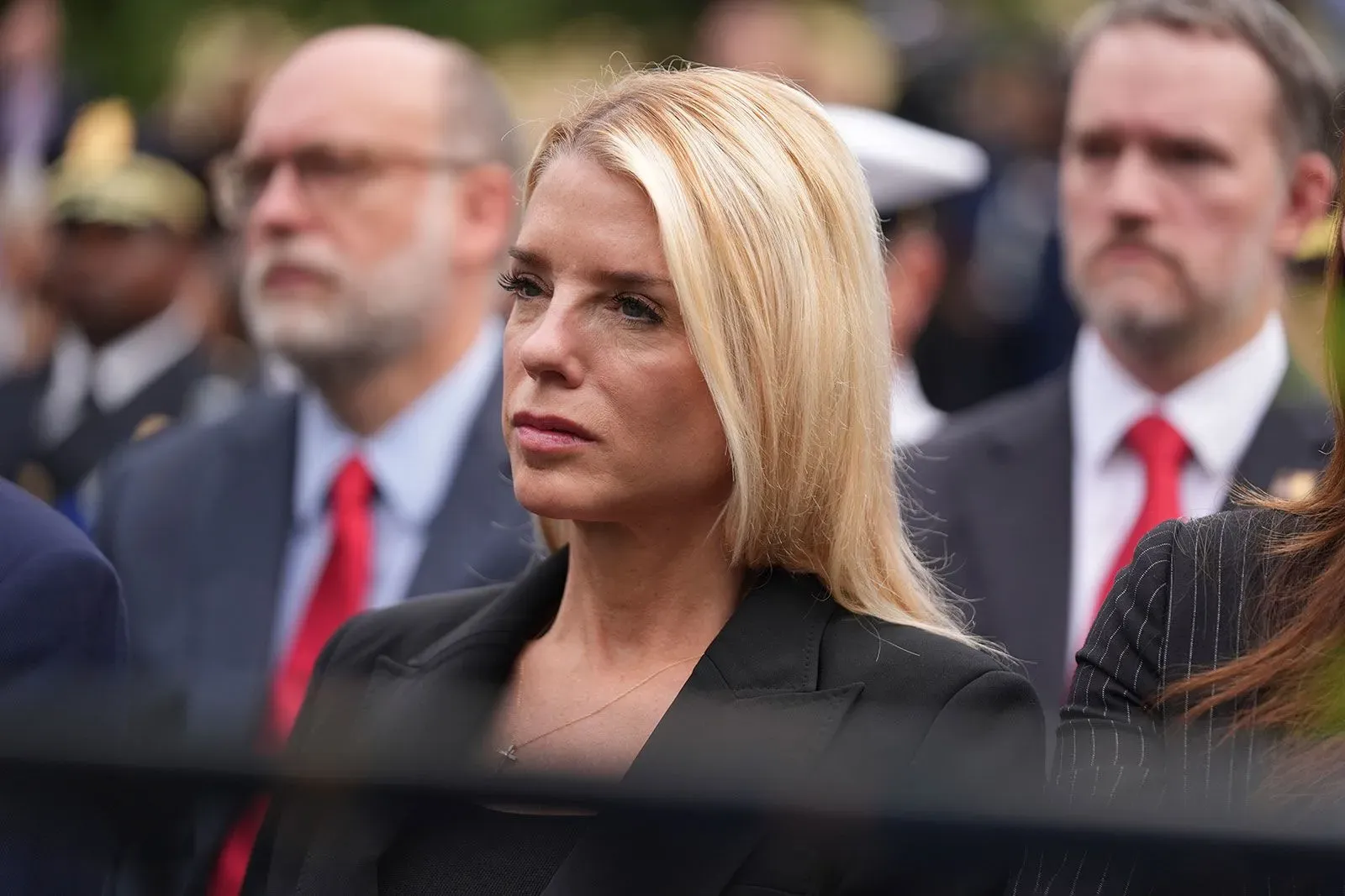 مدعي عام يرتدي ملابس سوداء، تبدو على وجهها ملامح القلق والتفكير، بينما تحضر فعالية رسمية وسط حشد من الناس.