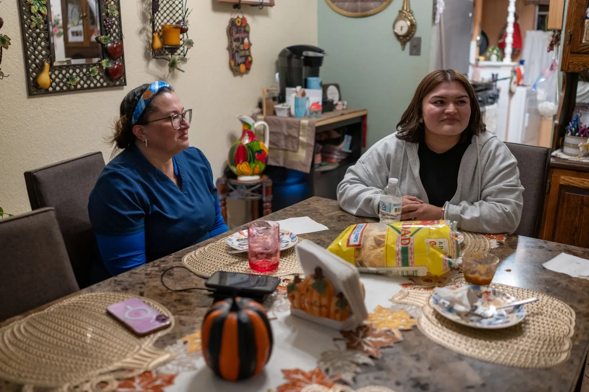 امرأتان تجلسان معًا على طاولة طعام، تتحدثان في أجواء منزلية دافئة، مع وجود مشروبات ووجبات خفيفة.