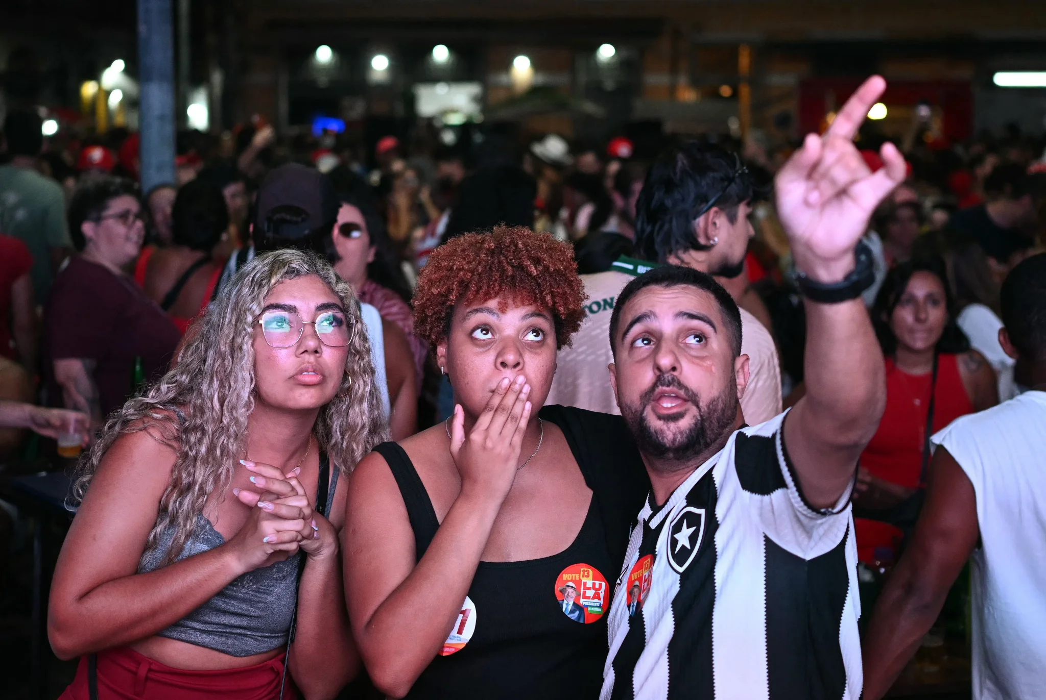 شبان برازيليون يراقبون نتائج الانتخابات وسط حشد، مع شعور بالتوتر والترقب في أجواء المنافسة الرئاسية بين لولا وبولسونارو.