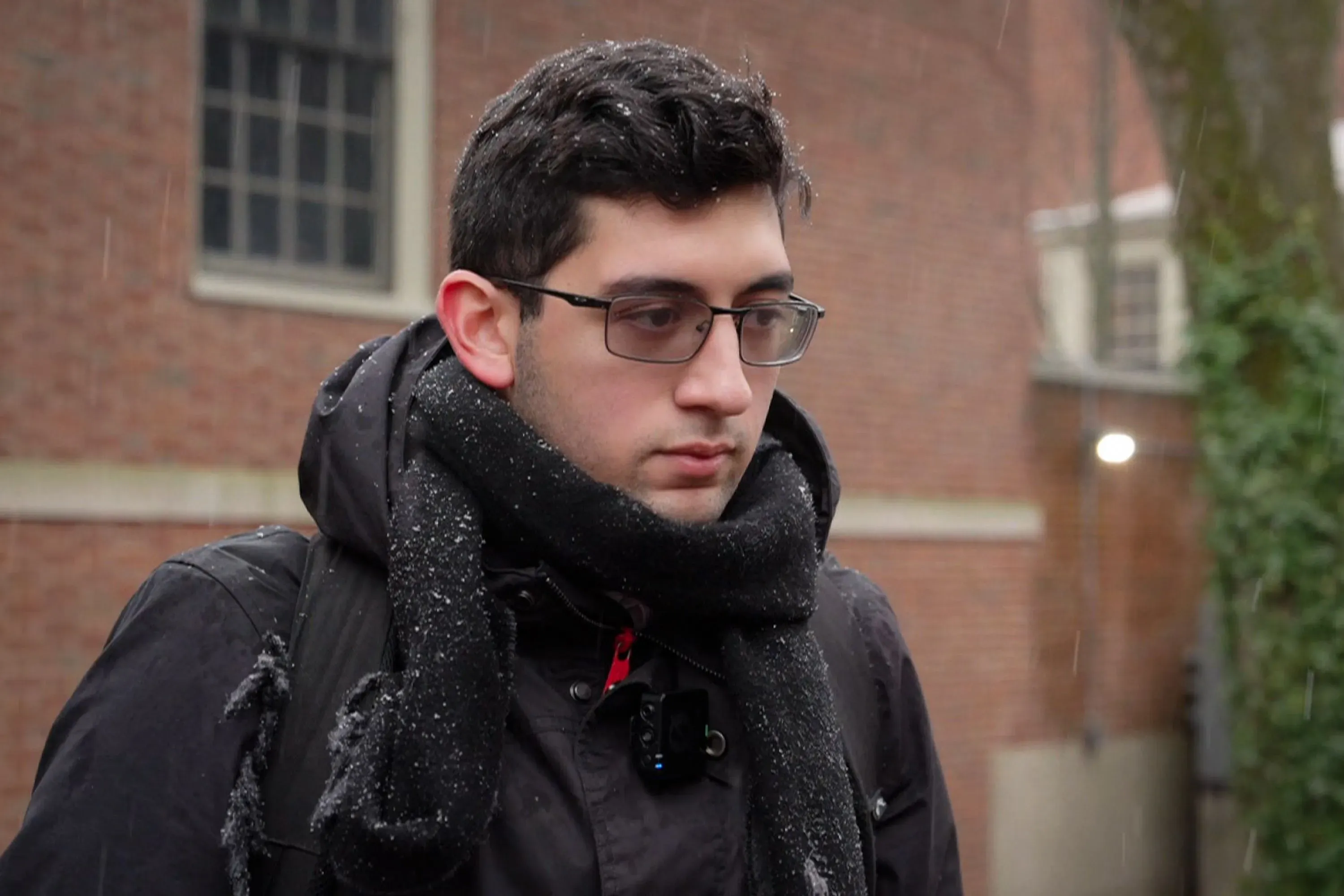 طالب يرتدي سترة داكنة وشال، يبدو عليه القلق أثناء تواجده في حرم جامعة براون بعد حادث إطلاق النار، وسط تساؤلات حول الأمن.