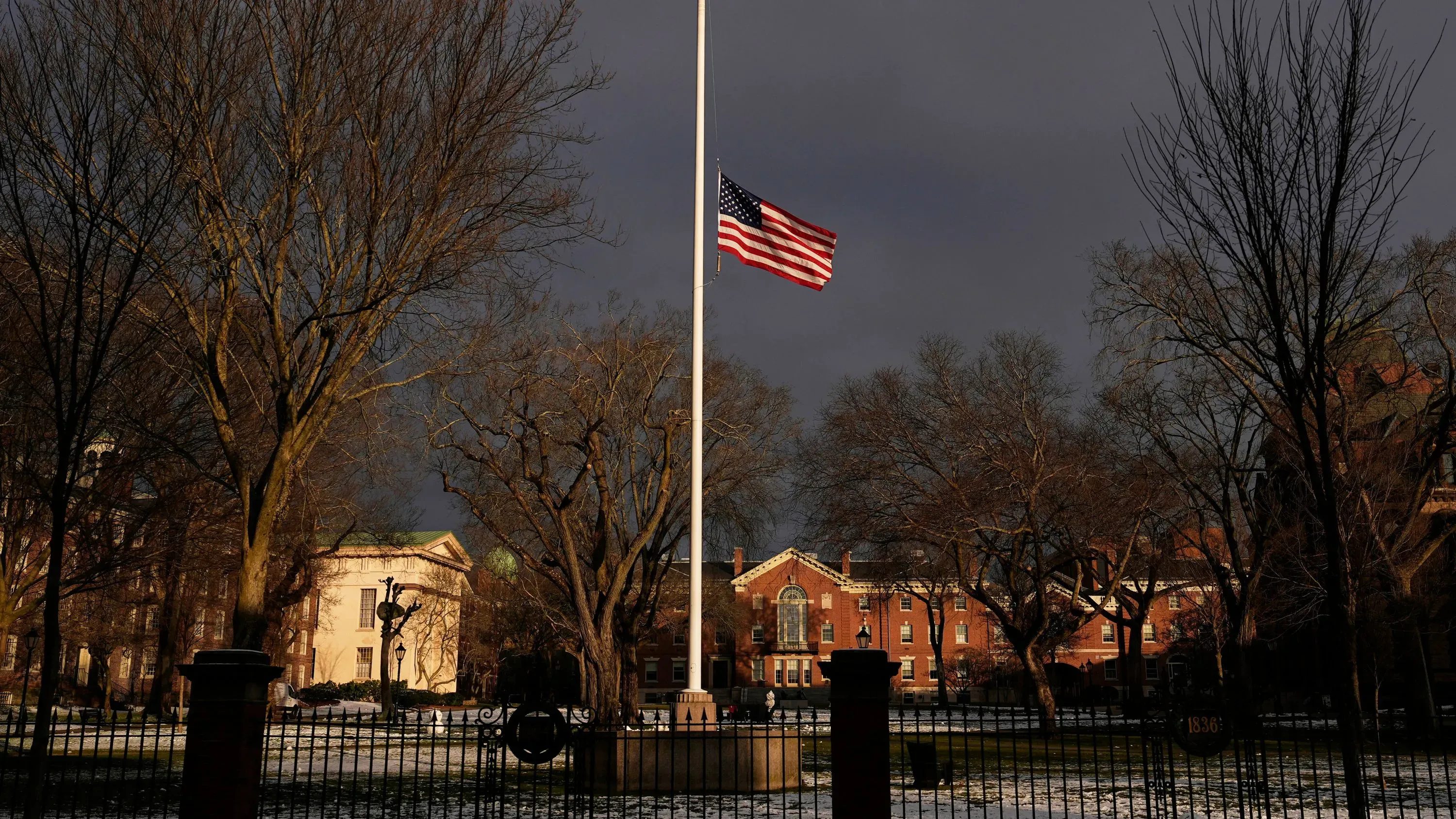 علم أمريكي مرفوع على سارية في حرم جامعة براون، محاط بأشجار عارية، في ظل أجواء قاتمة تعكس حالة الحزن بعد حادث إطلاق النار.