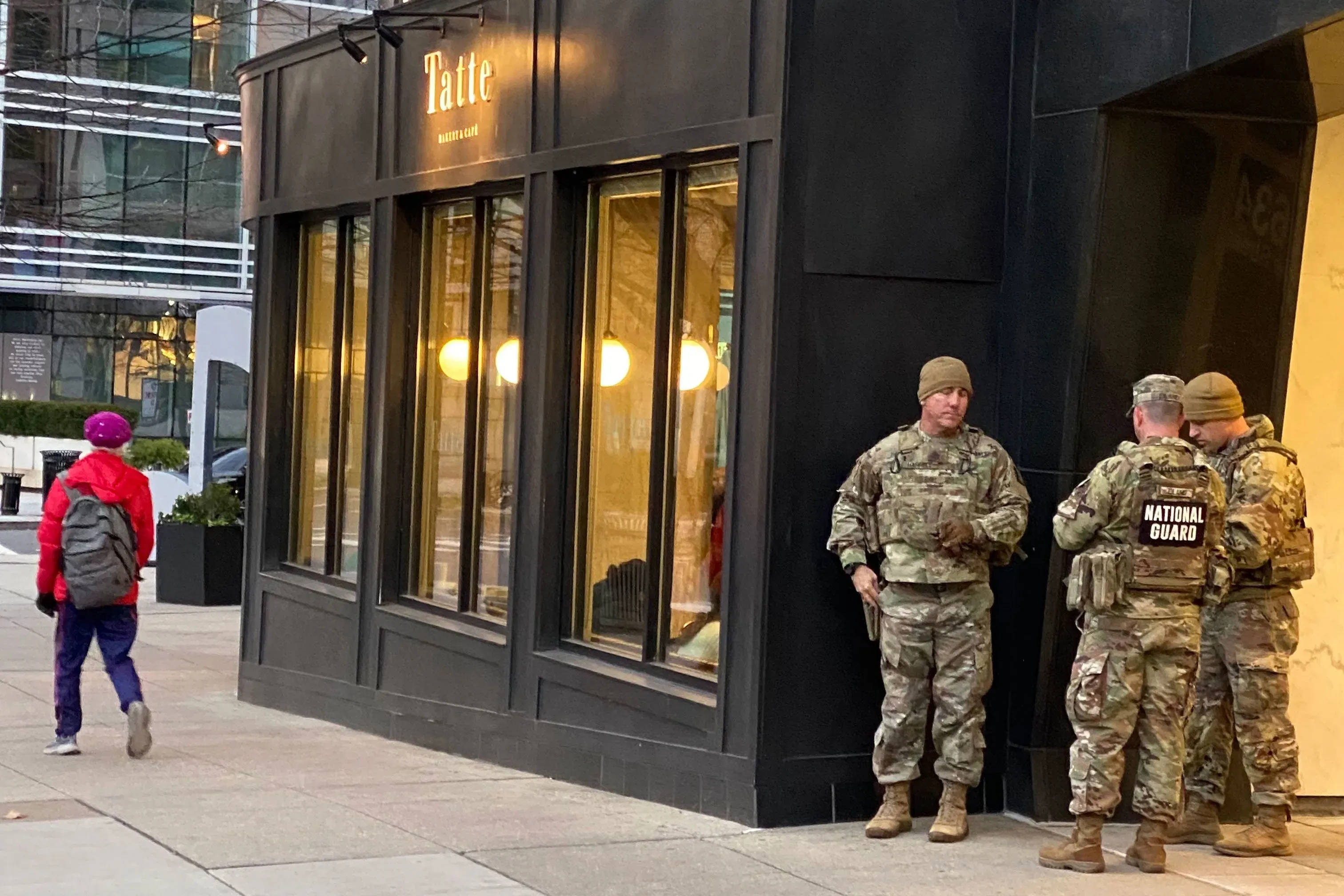 تجمع أفراد الحرس الوطني بالقرب من مقهى "تاتي" في واشنطن، مع وجود شخص يمشي في الخلفية، في سياق أحداث العنف الأخيرة.