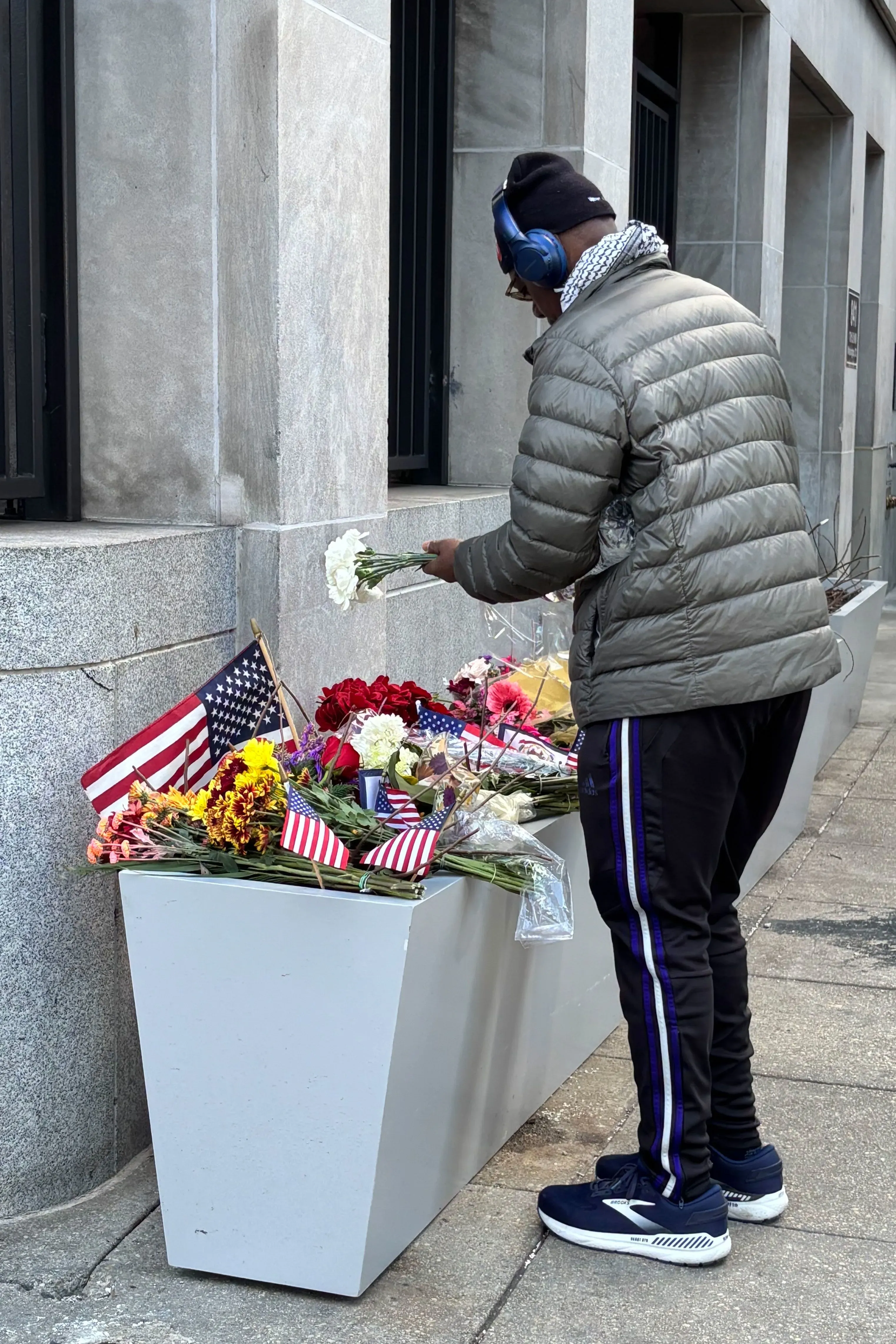 رجل يضع زهورًا عند نصب تذكاري يحمل أعلامًا أمريكية، تعبيرًا عن الحزن بعد مقتل سارة بيكستروم في حادث إطلاق نار.