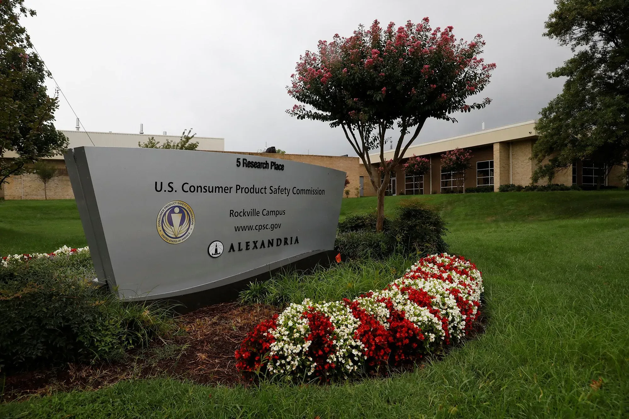 لافتة كبيرة لمفوضية سلامة المنتجات الاستهلاكية الأمريكية، مع حديقة مزهرة وأشجار في الخلفية، تعكس أهمية السلامة العامة.