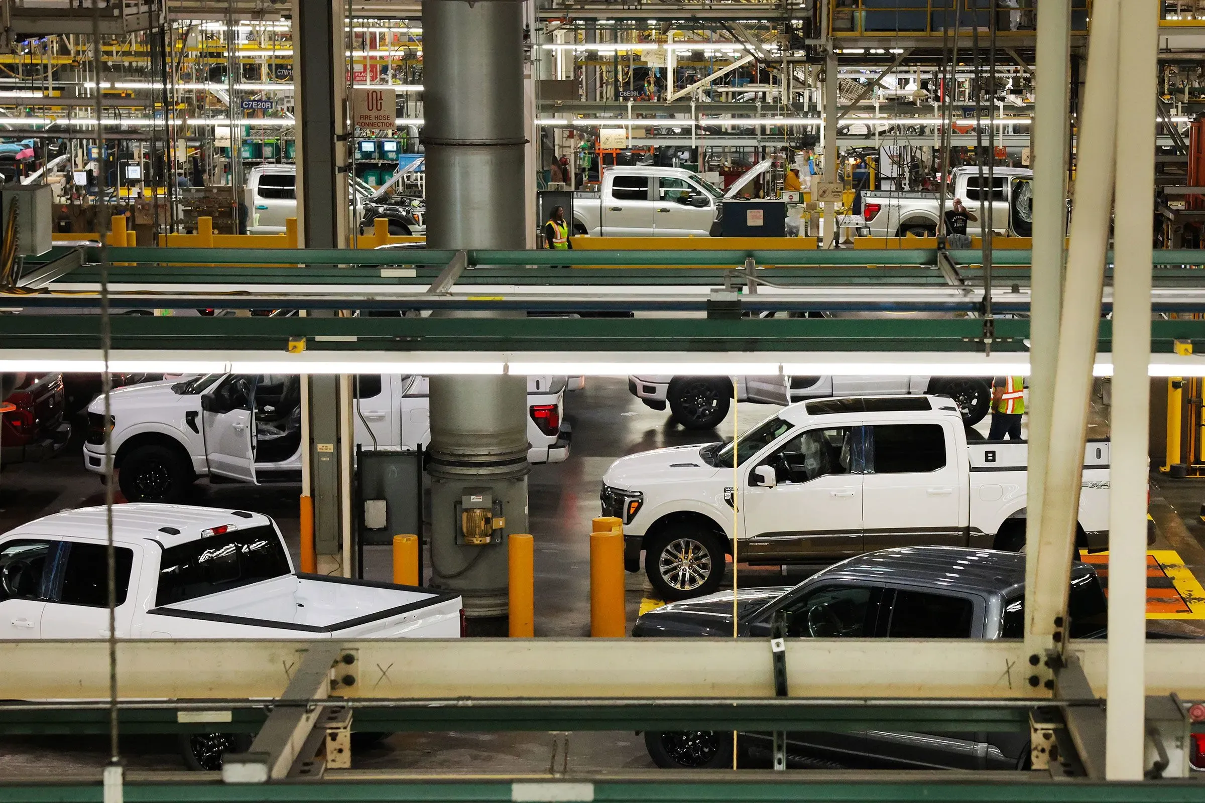 صورة لمصنع سيارات يظهر فيه مجموعة من الشاحنات البيضاء والسوداء أثناء عملية التجميع، مما يعكس التحديات التي تواجهها صناعة السيارات الأمريكية.