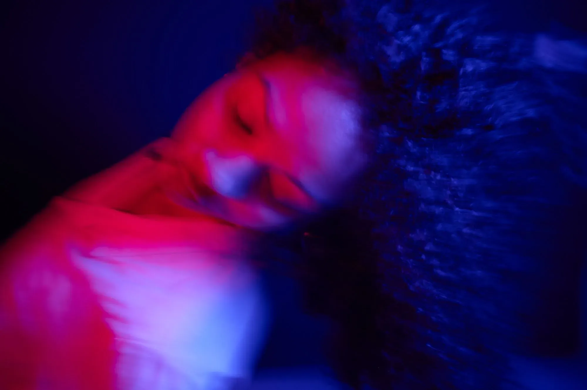 امرأة ذات شعر مجعد تتعرض لأضواء ملونة زاهية في بيئة غير واضحة، تعكس تجربة العلاج بالكيتامين وتأثيراته.