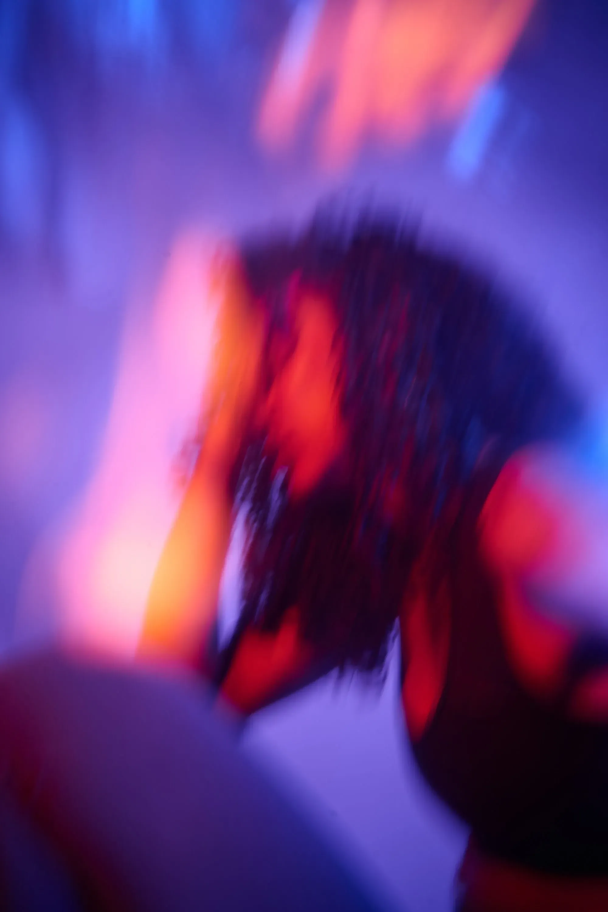 امرأة ذات شعر مجعد تجلس في بيئة مظلمة مضاءة بألوان زاهية، تعبر عن مشاعر القلق أو الارتباك، مما يعكس تأثيرات الكيتامين على الصحة العقلية.