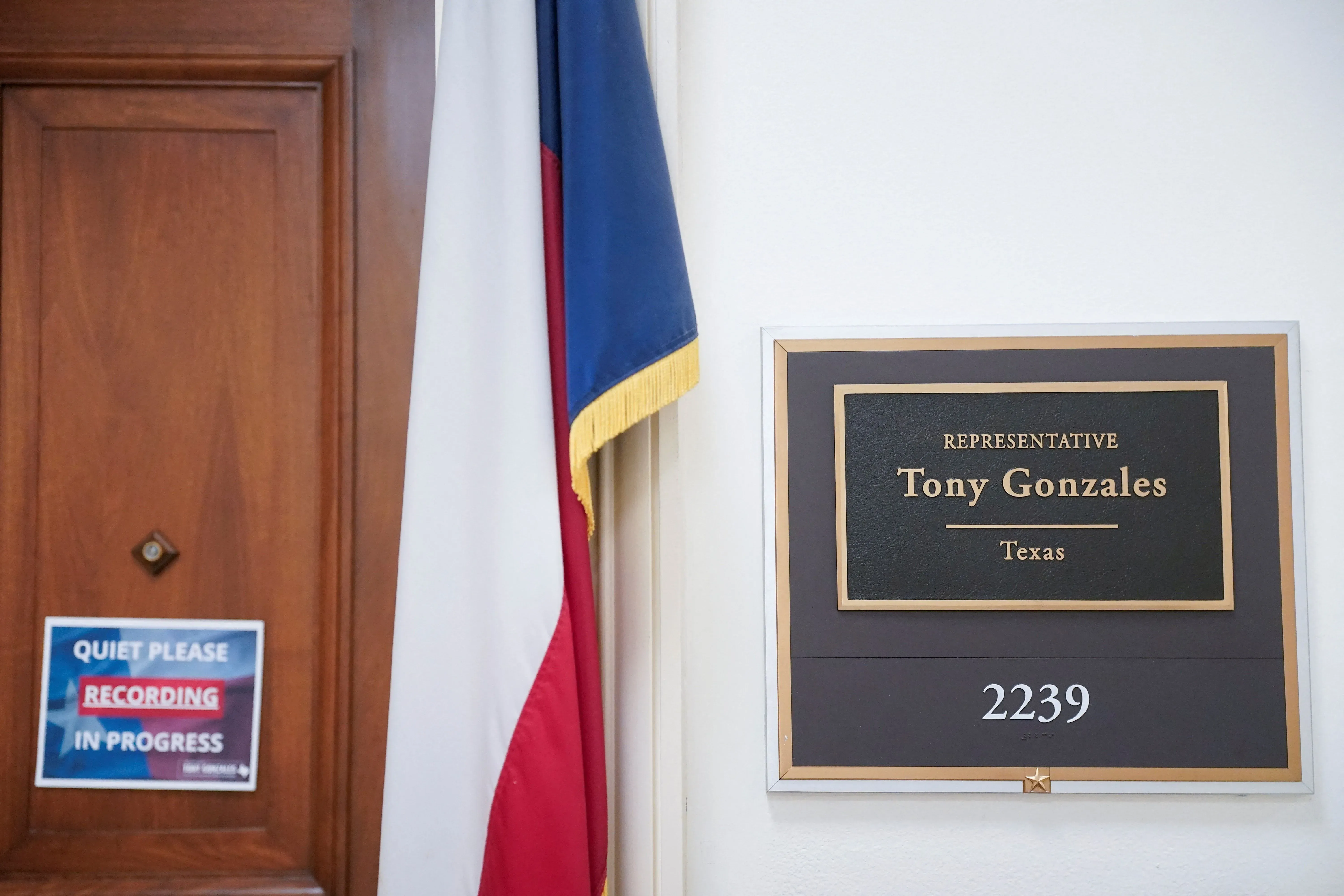 لافتة تحمل اسم النائب توني غونزاليس، مع العلم الأمريكي، أمام باب مكتبه في الكونغرس، تعكس أجواء التوتر بعد استقالته.