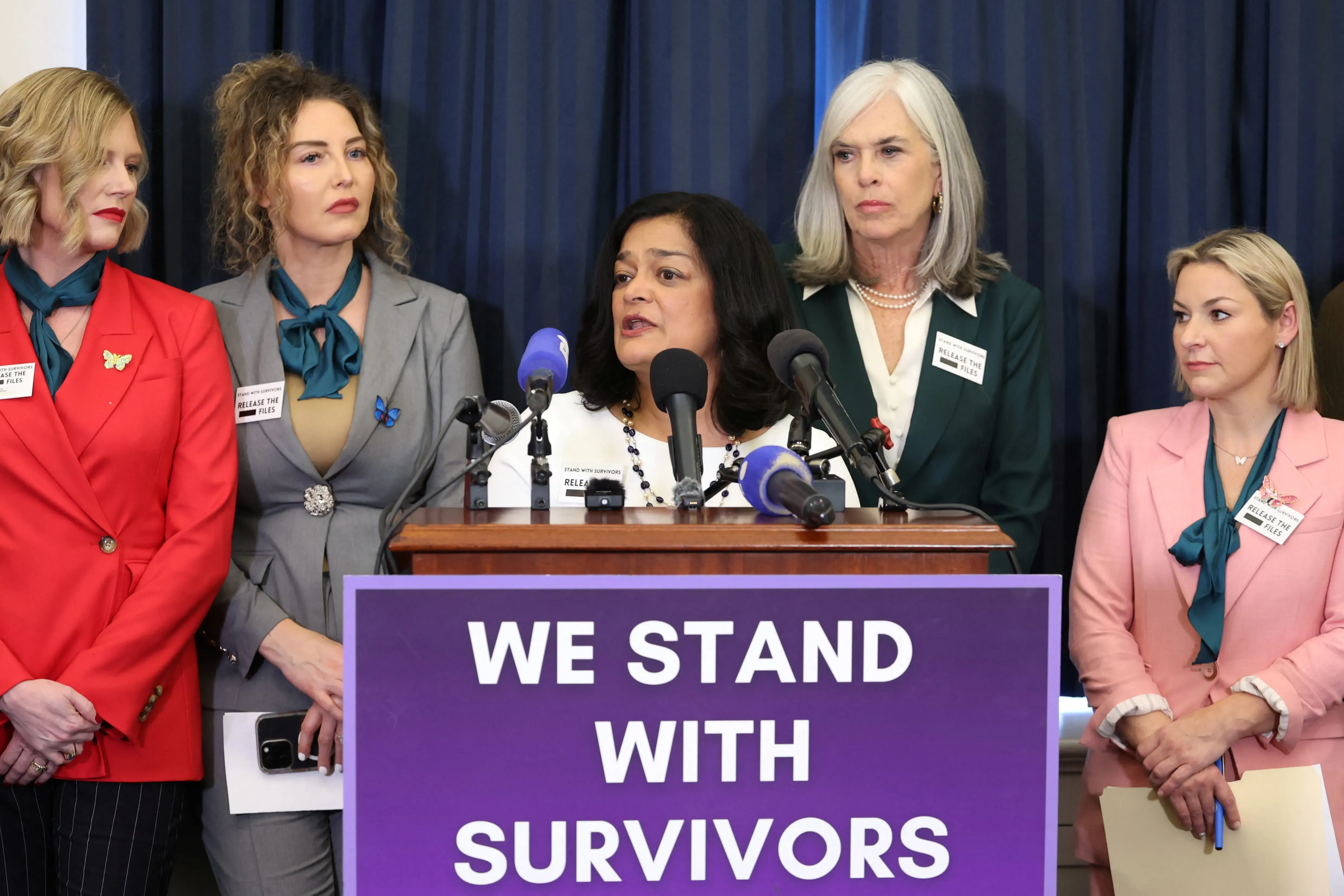 خمس نساء يقفن أمام ميكروفونات، تتحدث إحداهن عن دعم الناجين من الاعتداءات الجنسية، مع لافتة "نحن نقف مع الناجين" خلفهن.