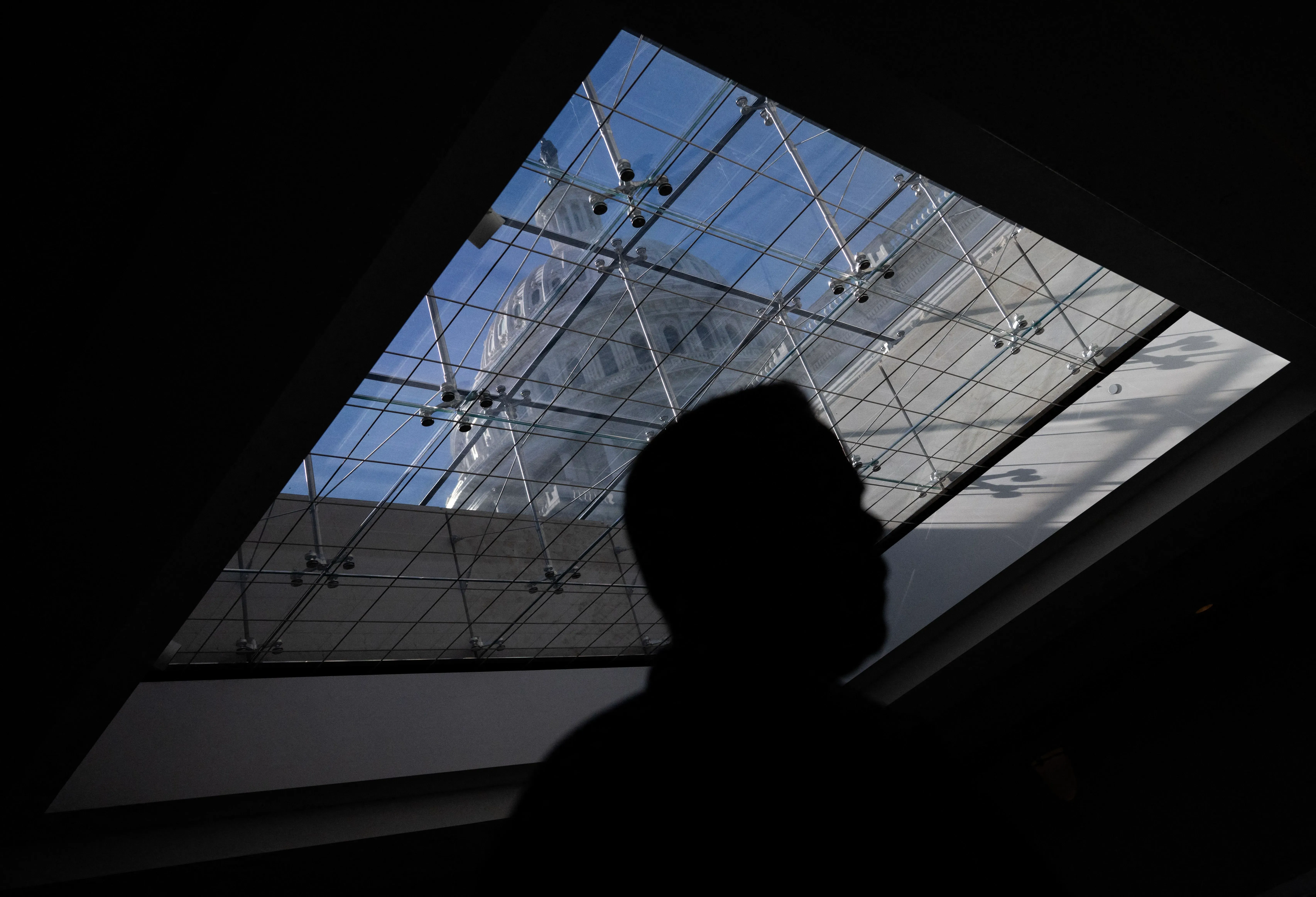 ظل شخص silhouetted أمام سقف زجاجي يظهر مبنى الكونغرس، مما يعكس التوترات السياسية والفضائح المتعلقة بسوء السلوك في الأروقة الحكومية.