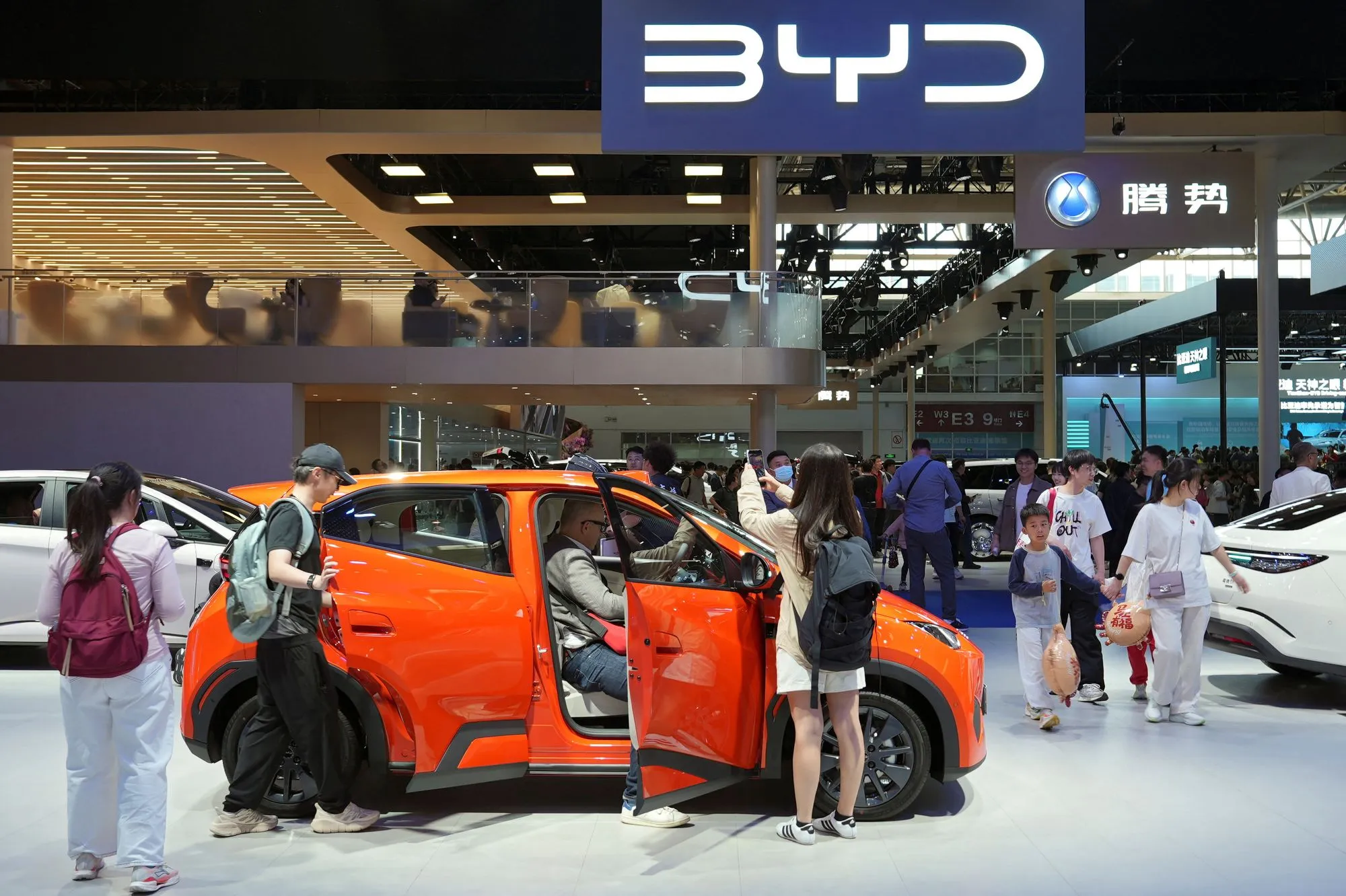زوار معرض سيارات صيني يتفقدون سيارة كهربائية برتقالية من علامة BYD وسط اهتمام متزايد بتقنيات السيارات الخضراء والصادرات الصينية.