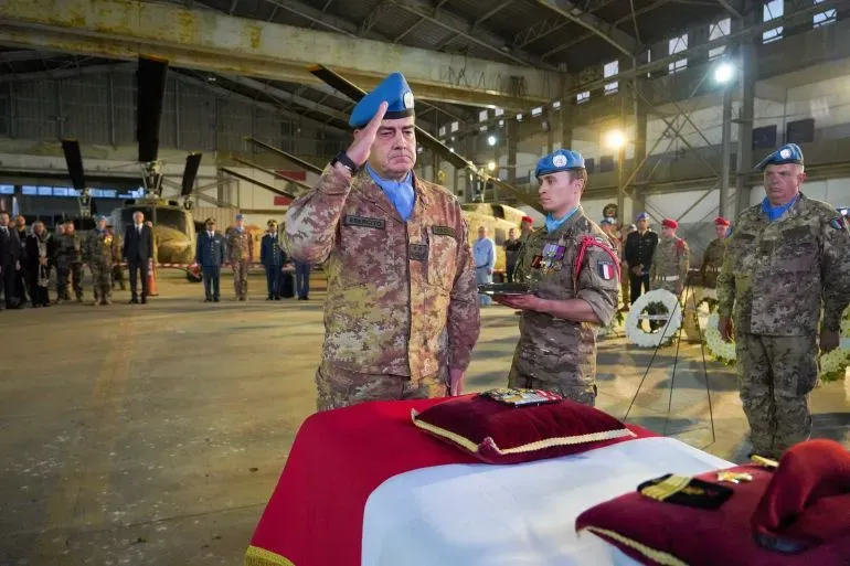 تحتوي الصورة على جنود من قوة الأمم المتحدة المؤقتة في لبنان (UNIFIL) أثناء مراسم تأبين، حيث يقوم أحدهم بتحية عسكرية أمام نعش مغطى بالعلم.