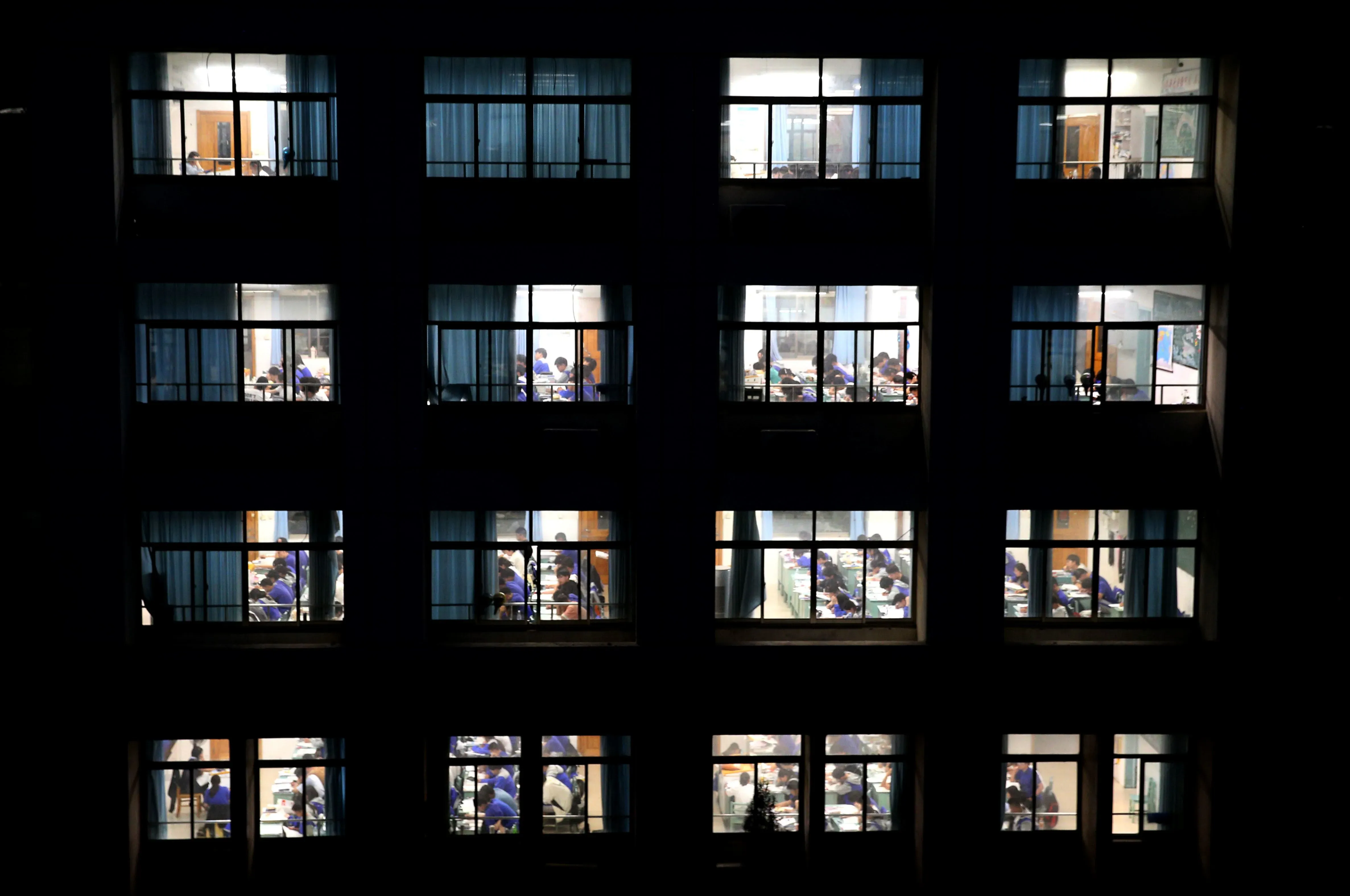 طلاب يدرسون في فصول مضاءة داخل مبنى ليلي في الصين، يعكس التحديات التعليمية والضغوط التي يواجهها الشباب.