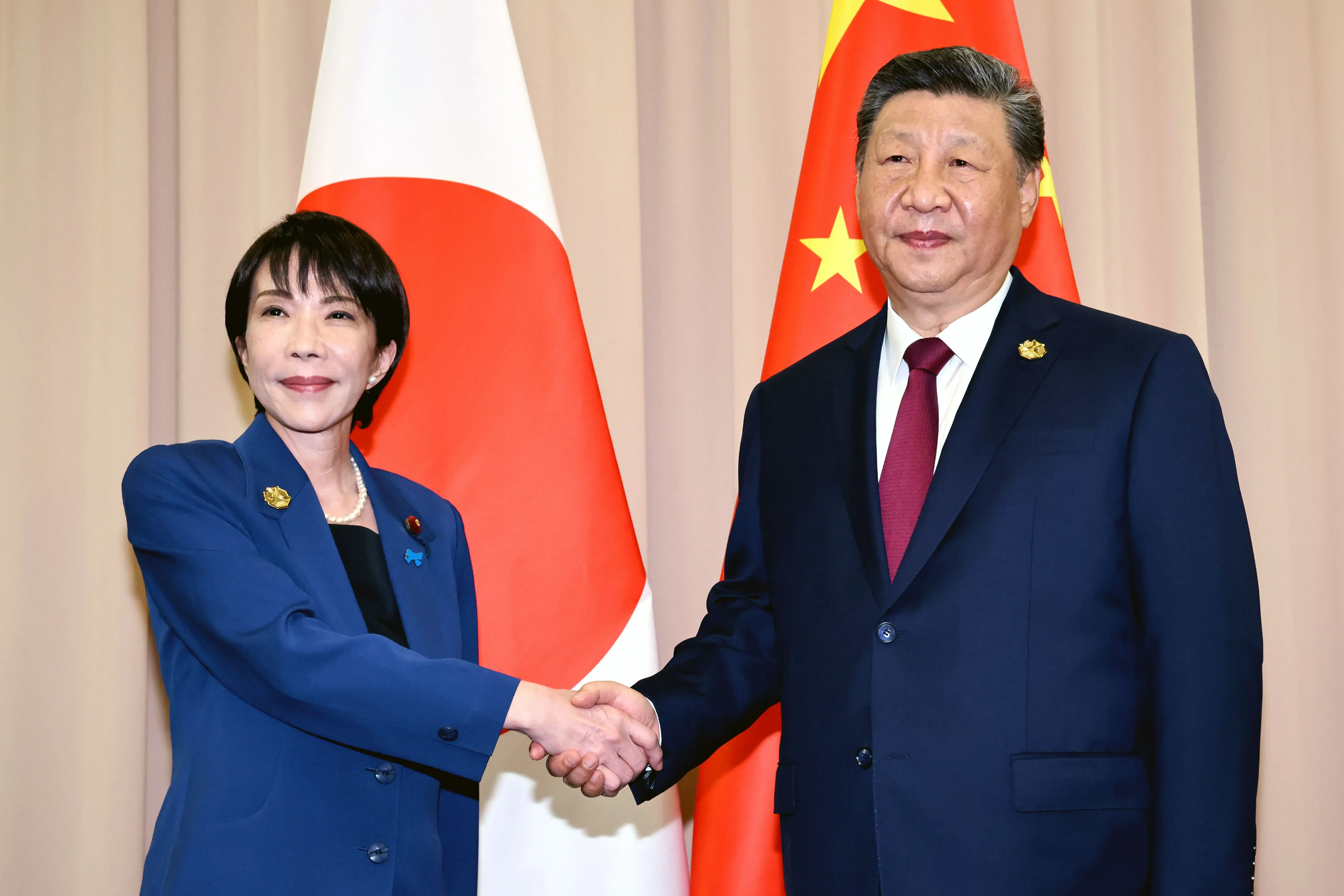 اجتماع بين رئيسة وزراء اليابان ساني تاكايتشي والرئيس الصيني شي جين بينغ، حيث يتصافحان وسط أعلام البلدين.