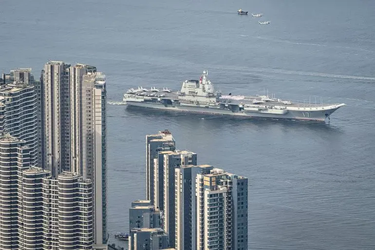 حاملة الطائرات الصينية "لياونينغ" تبحر في مياه المحيط الهادئ، محاطة بناطحات السحاب، في إطار تعزيز القدرات البحرية الصينية.