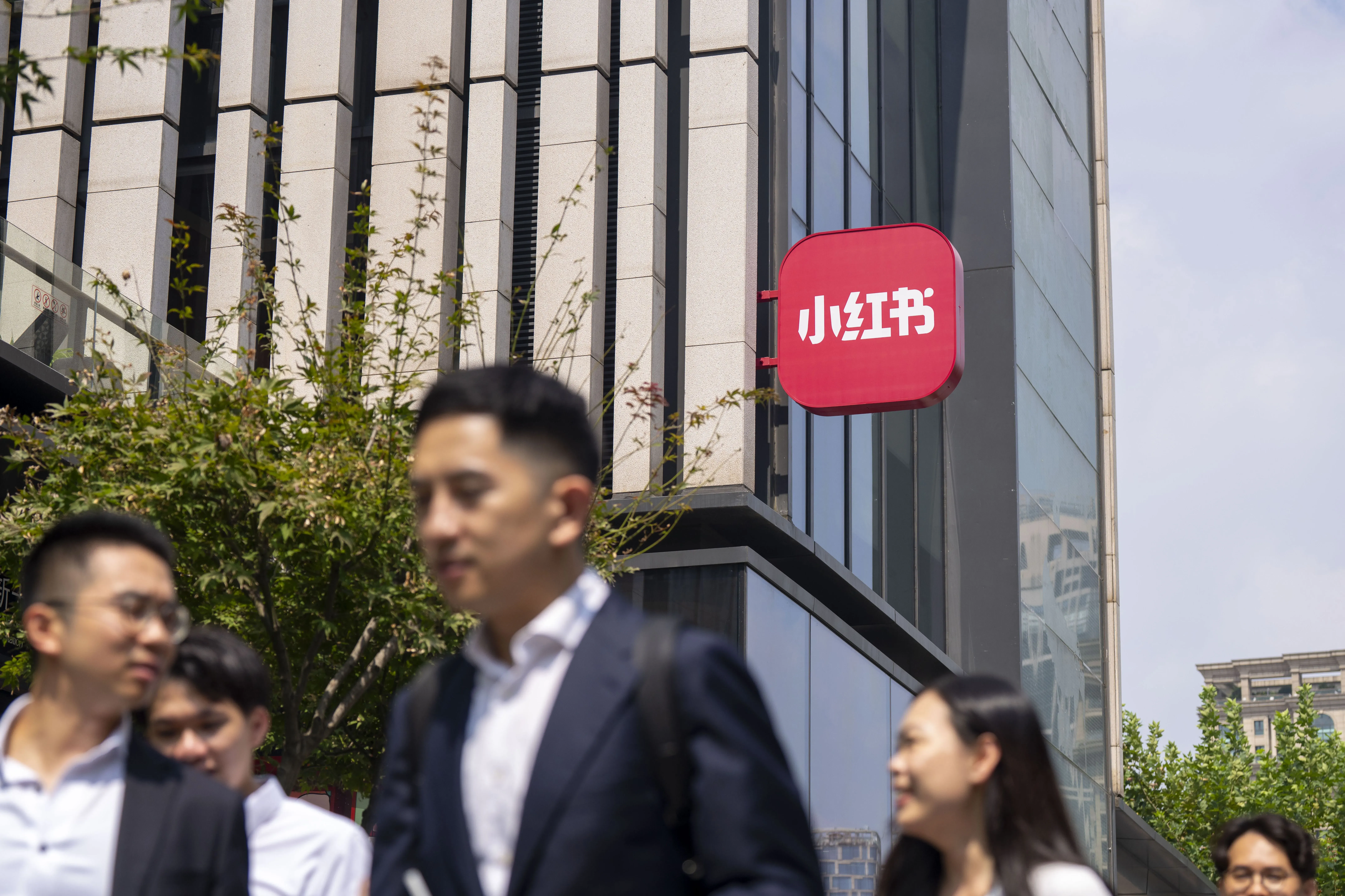 شعار منصة "شياوهونغشو" يبرز على واجهة مبنى حديث، مع مجموعة من الأشخاص يسيرون في الشارع، مما يعكس النشاط الاجتماعي في الصين.