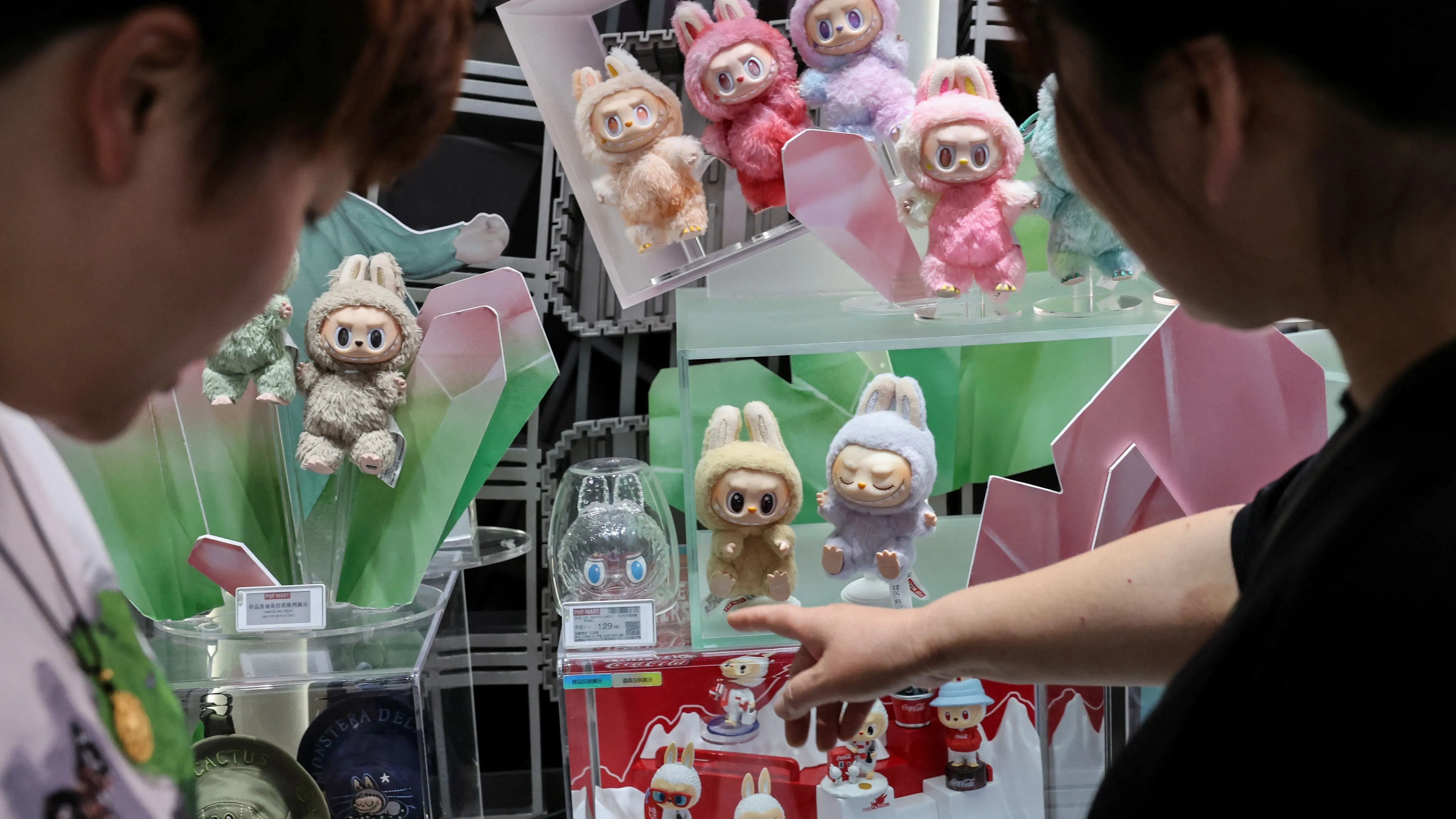 نساء تتفحصن مجموعة من دمى "لافوفو" الملونة في متجر، مع التركيز على التفاصيل الفريدة لكل دمية.