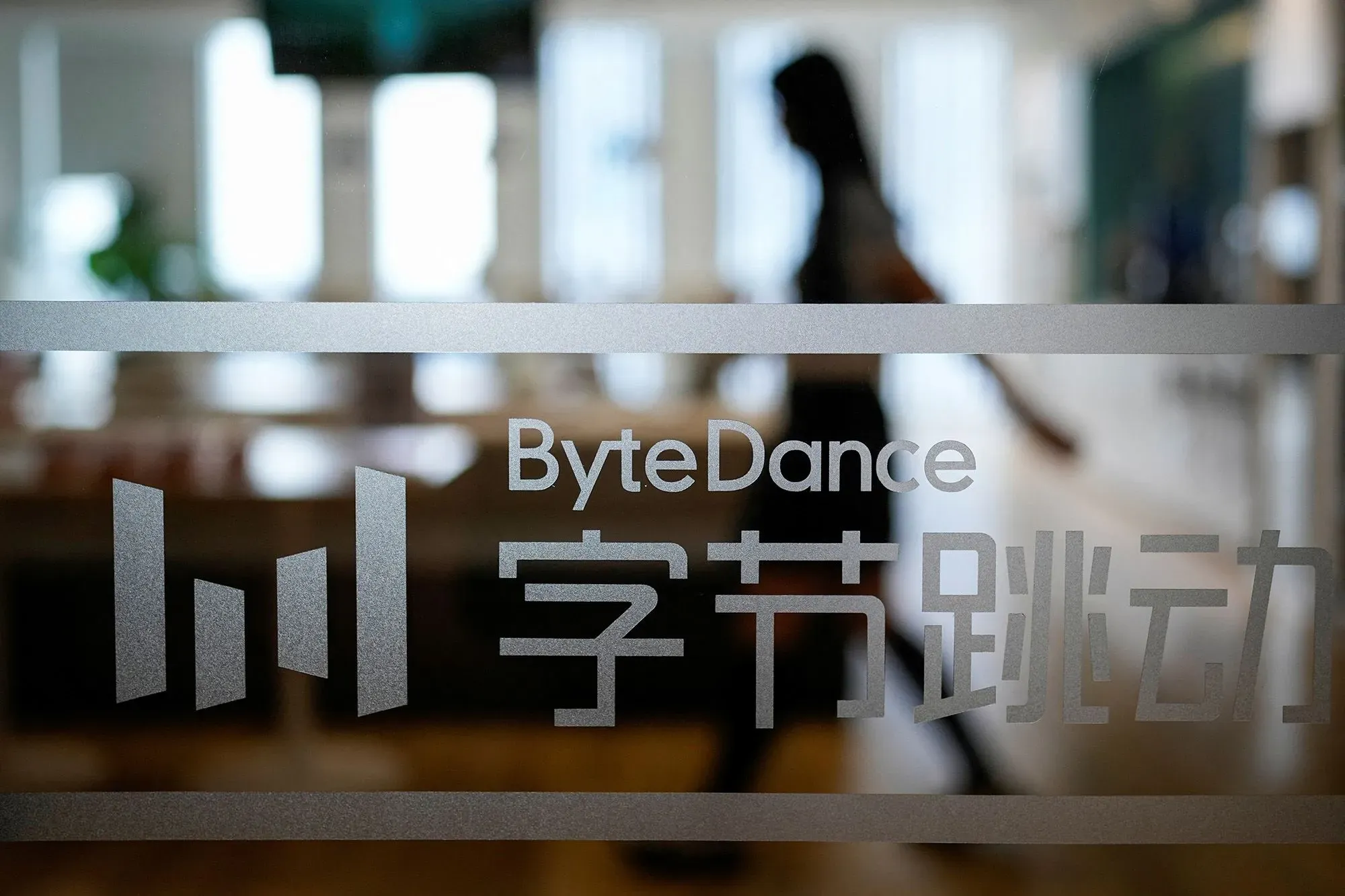 شعار شركة ByteDance يظهر على زجاج مكتب، مع شخص يتحرك في الخلفية، مما يعكس التطورات في تكنولوجيا الذكاء الاصطناعي.