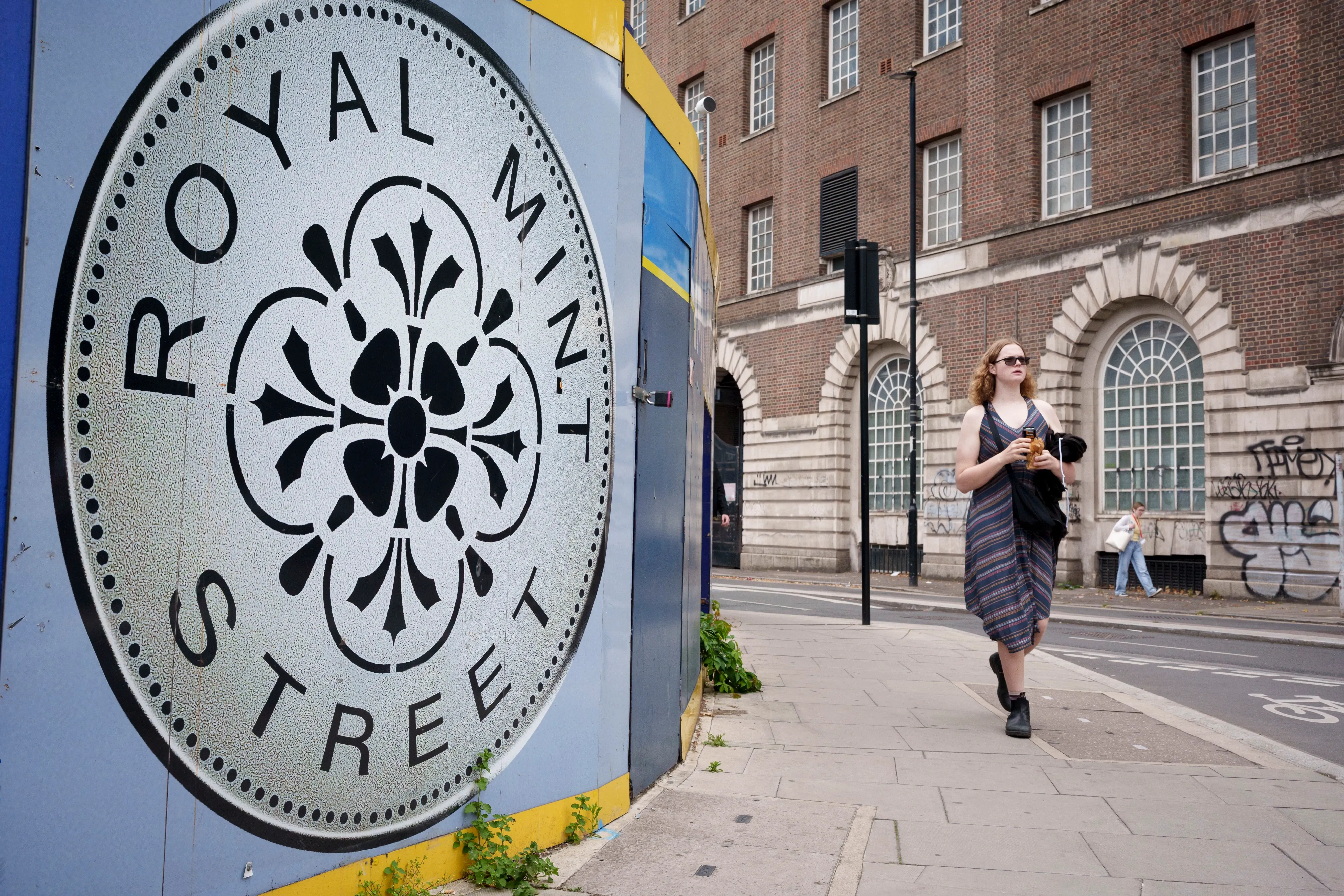 امرأة تمشي على رصيف شارع رويال مينت، بجوار لافتة كبيرة تحمل اسم الشارع، مع مبنى تاريخي في الخلفية.