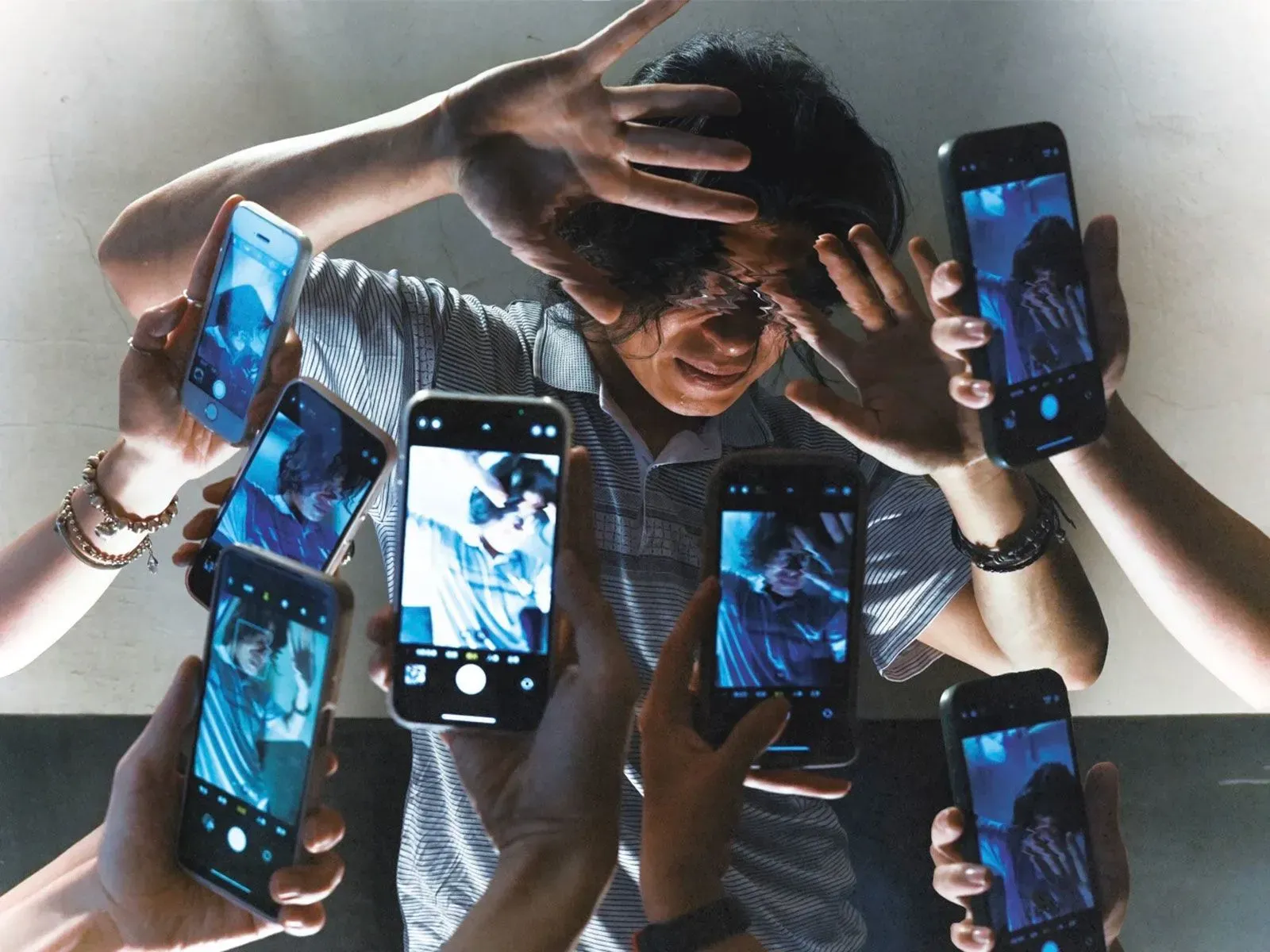 صورة تُظهر شابًا يحاول حماية وجهه بينما تُوجه إليه عدة هواتف تُسجل مقاطع فيديو، تعبيرًا عن انتهاك الخصوصية.