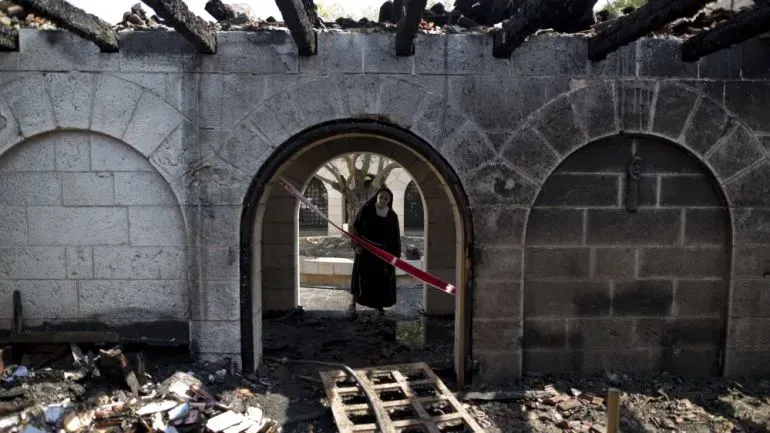 امرأة ترتدي ملابس دينية تقف داخل كنيسة متضررة من الحريق، مع آثار الدمار حولها، مما يعكس التحديات التي تواجه المجتمعات المسيحية في فلسطين.