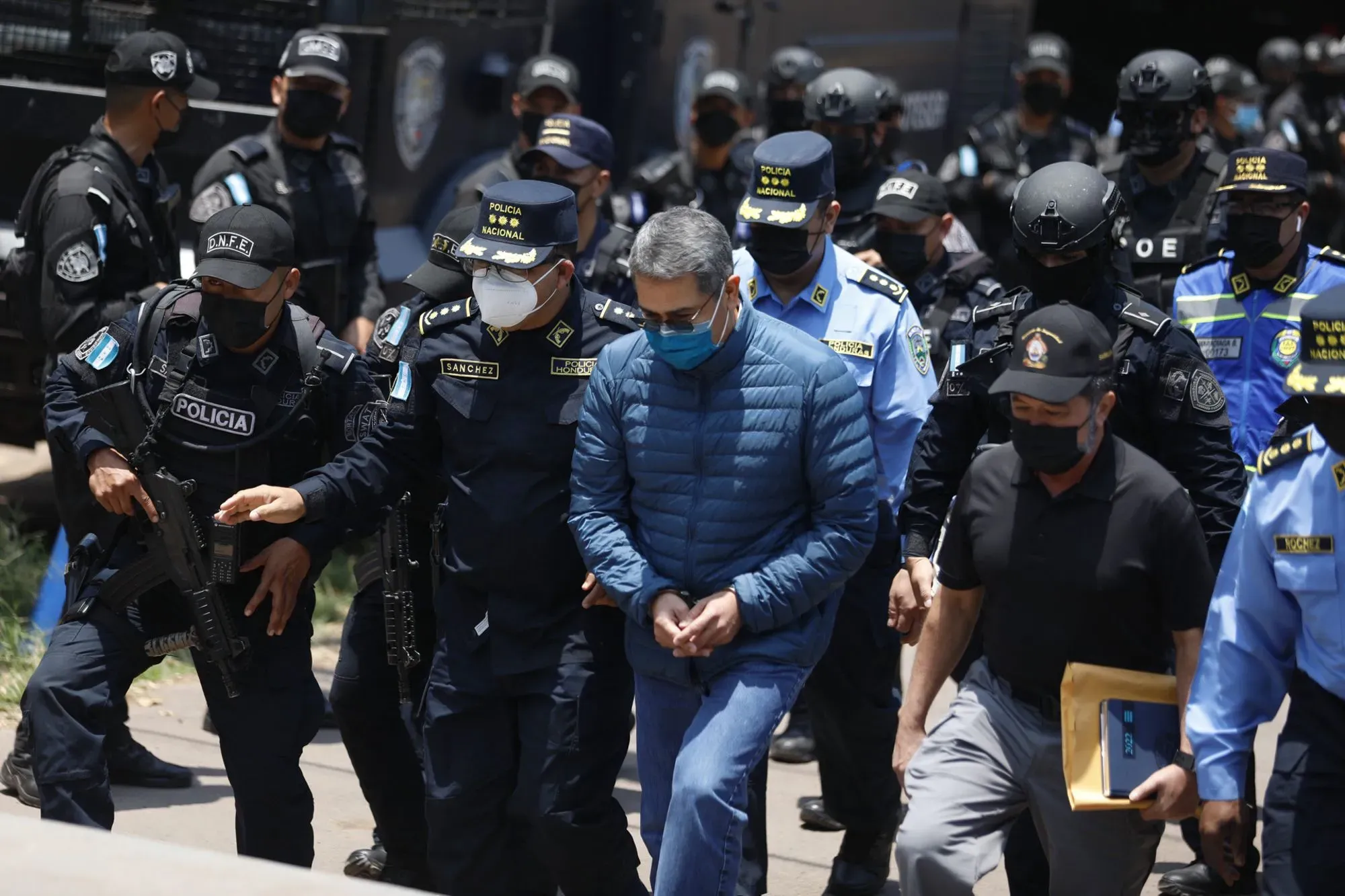 اعتقال شخصية سياسية وسط حراسة مشددة من الشرطة، مع وجود عناصر أمنية مسلحة في الخلفية، مما يعكس التوترات الأمنية في المنطقة.