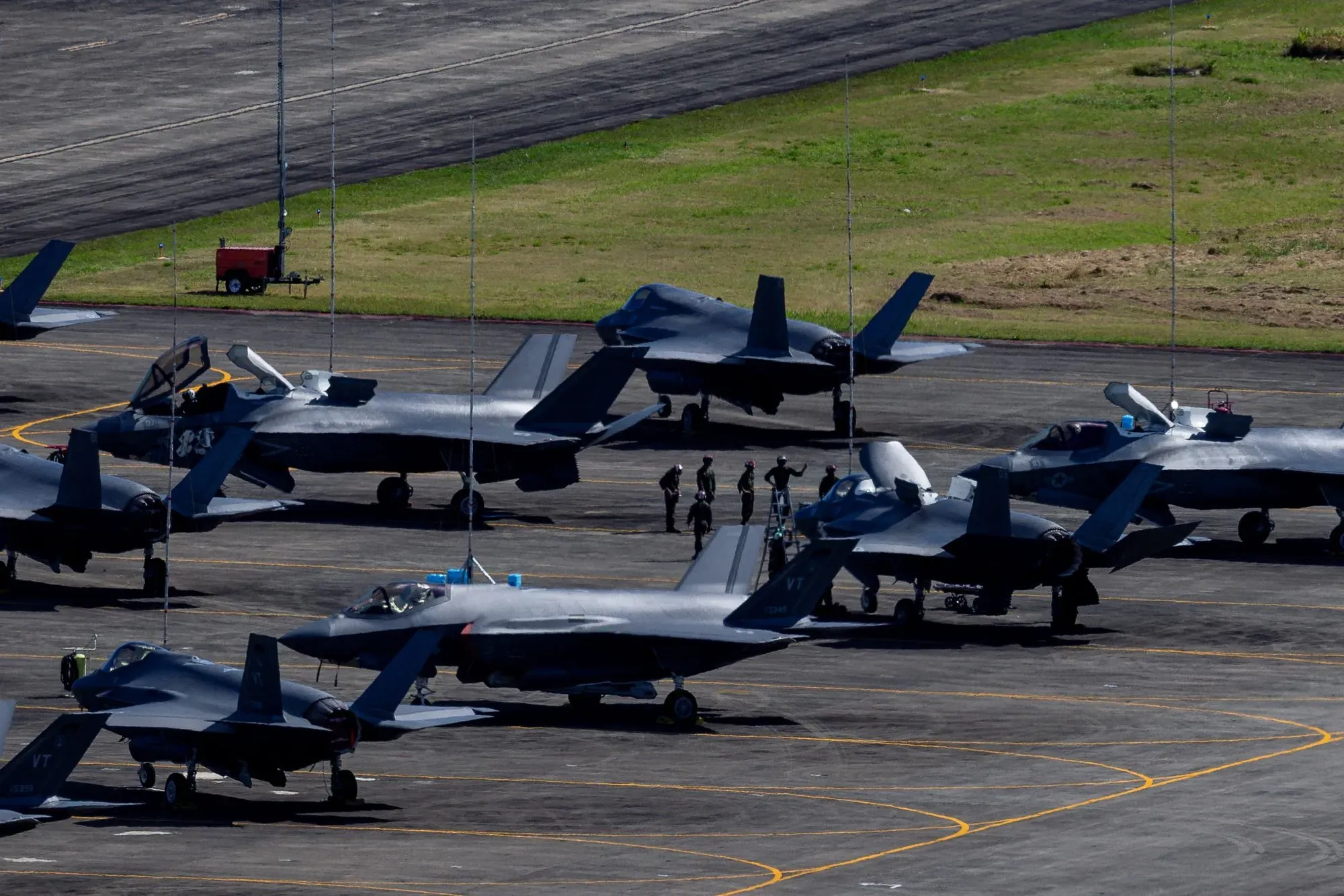 طائرات حربية متوقفة في قاعدة عسكرية، مع وجود أفراد من القوات المسلحة، تعكس تصعيد التوترات في السياسة الأمريكية تجاه فنزويلا.