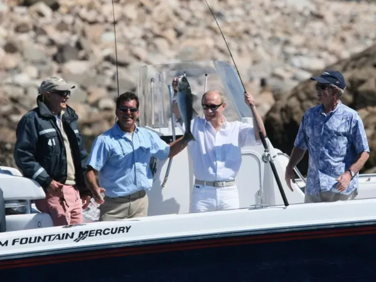 بوتين يحمل سمكة كبيرة خلال رحلة صيد مع مسؤولين أمريكيين، مما يعكس العلاقات الشخصية بين القادة وسط توترات سياسية.