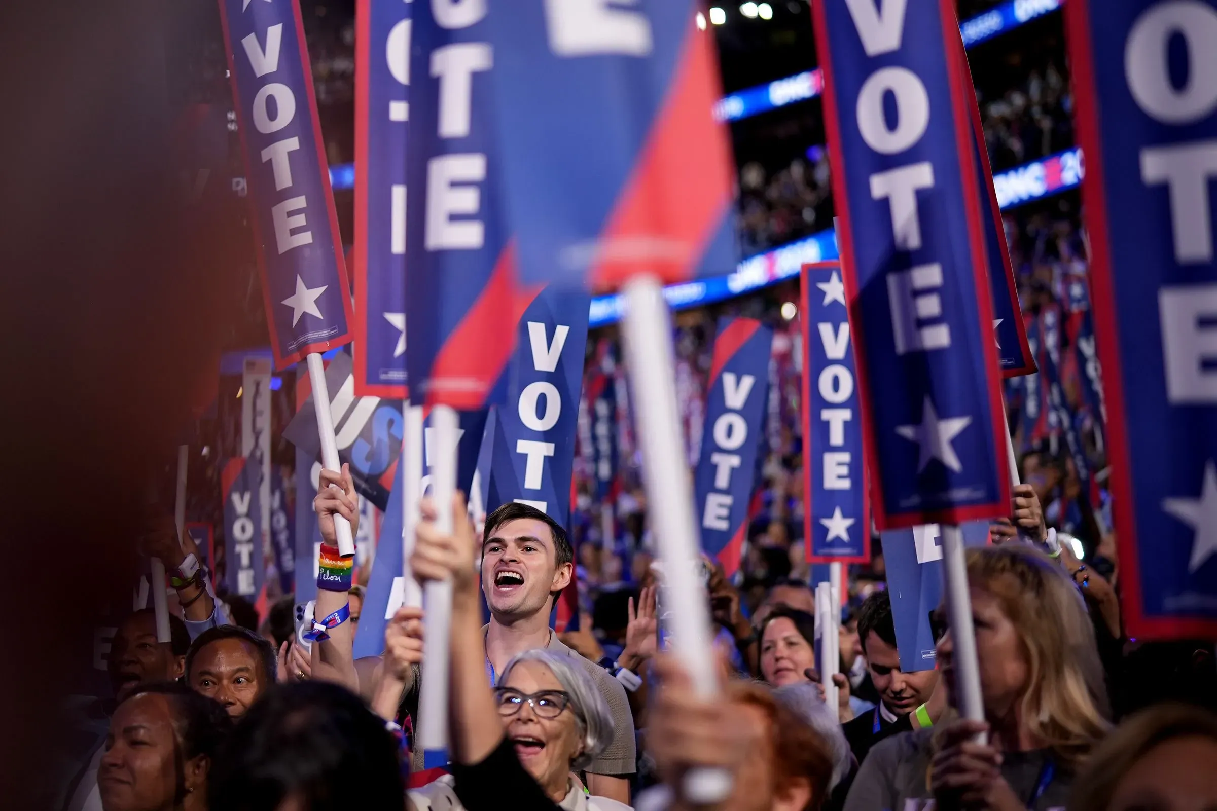 حشد من الناخبين يحملون لافتات "صوت" في تجمع سياسي، مع تعبيرات حماسية تدل على دعمهم للحزب الديمقراطي قبل انتخابات الكونغرس.