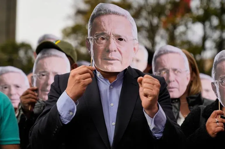 محتجون يحملون أقنعة تمثل الرئيس الكولومبي السابق ألفارو أوريبي، تعبيرًا عن دعمهم له بعد إدانته بالتلاعب بالشهود.