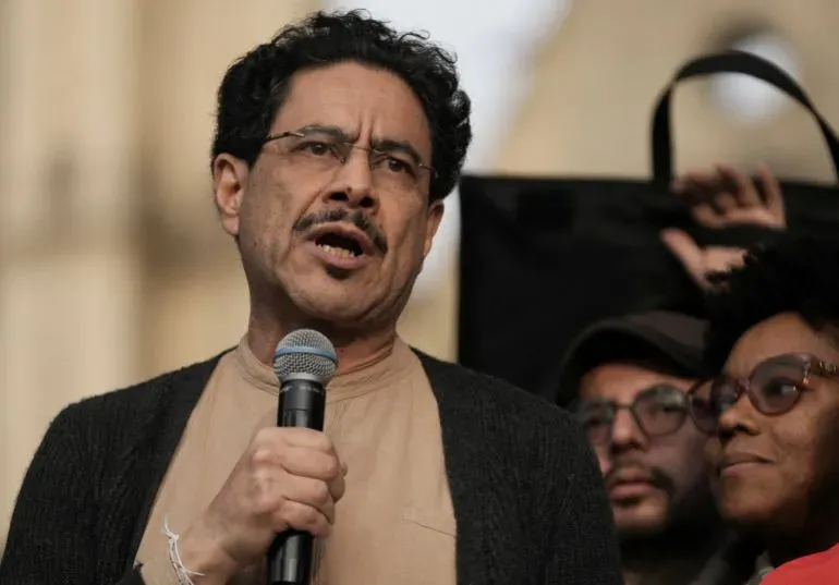 رجل يتحدث إلى حشد خلال تجمع، مع التركيز على تعبيراته الجادة. يُظهر الصورة النقاش حول التحقيقات المتعلقة بالرئيس الكولومبي بيترو.