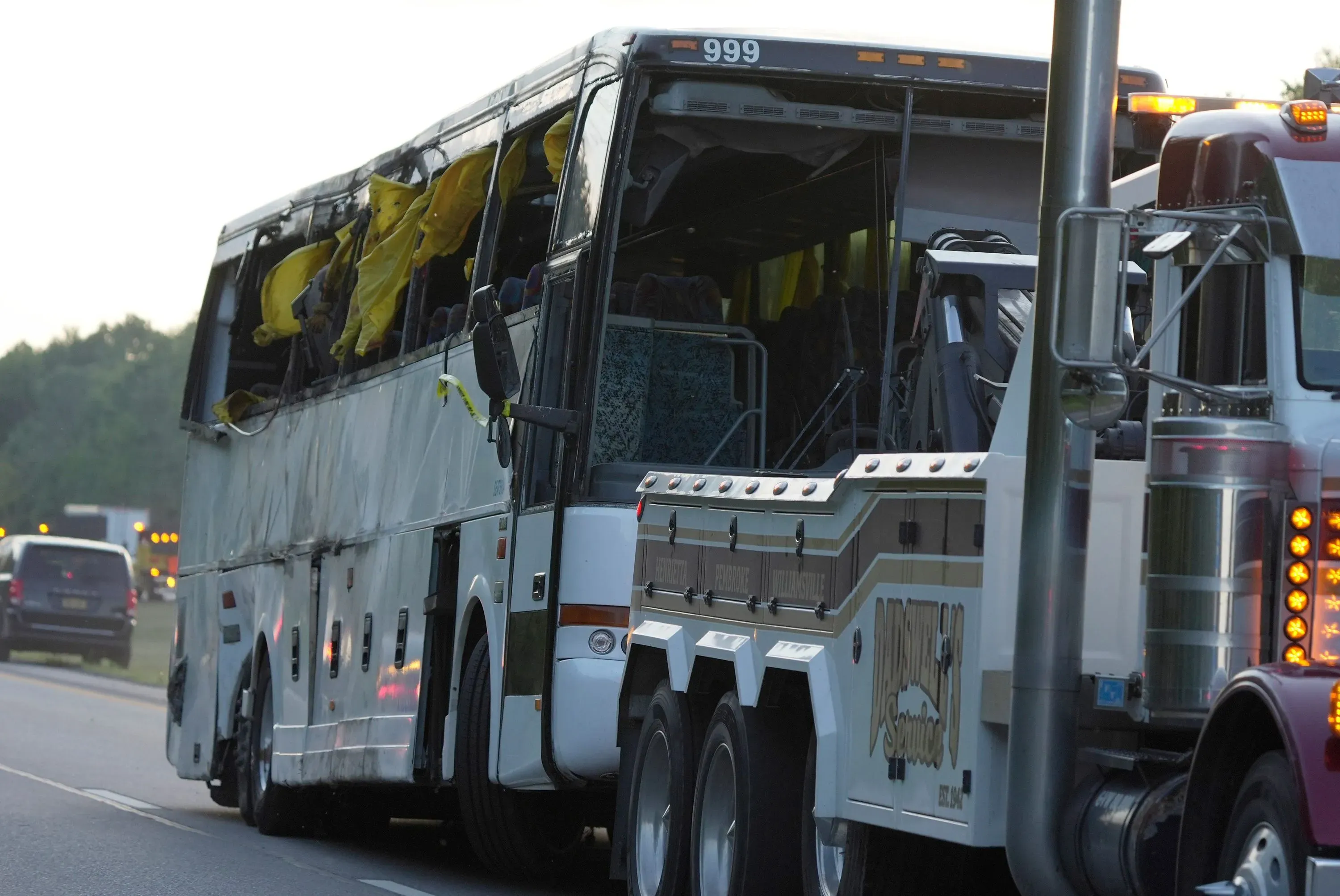 حافلة سياحية مقلوبة على جانب الطريق بعد حادث مروري، مع وجود حطام وممتلكات مبعثرة، مما يعكس خطورة الحادث.