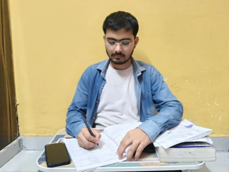 شاب يجلس على مكتب يدرس بجد، محاطًا بكُتب الكيمياء والملاحظات، يعكس طموحه في اجتياز اختبار NEET للدخول إلى كلية الطب.