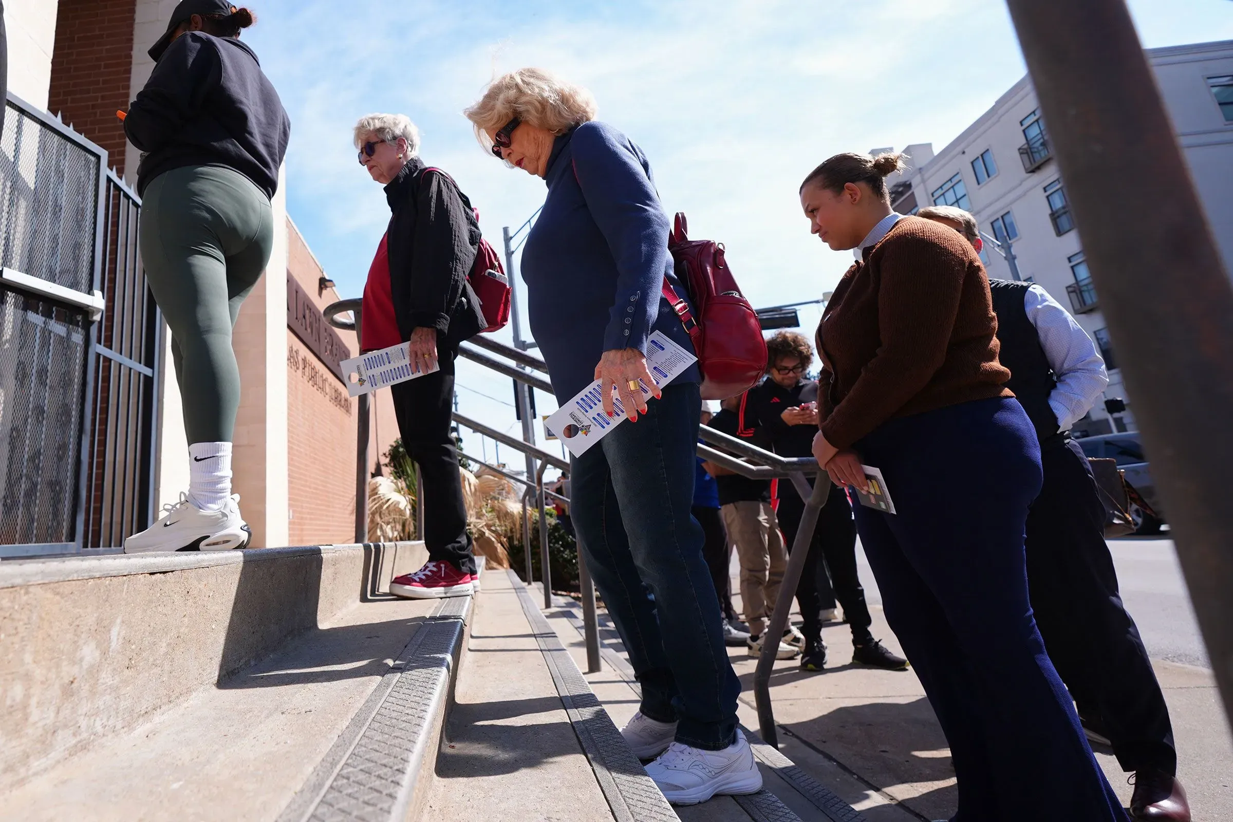 ناخبون يتجهون نحو مركز الاقتراع في تكساس، يحملون منشورات دعائية، وسط أجواء مشمسة، استعدادًا للانتخابات التمهيدية.