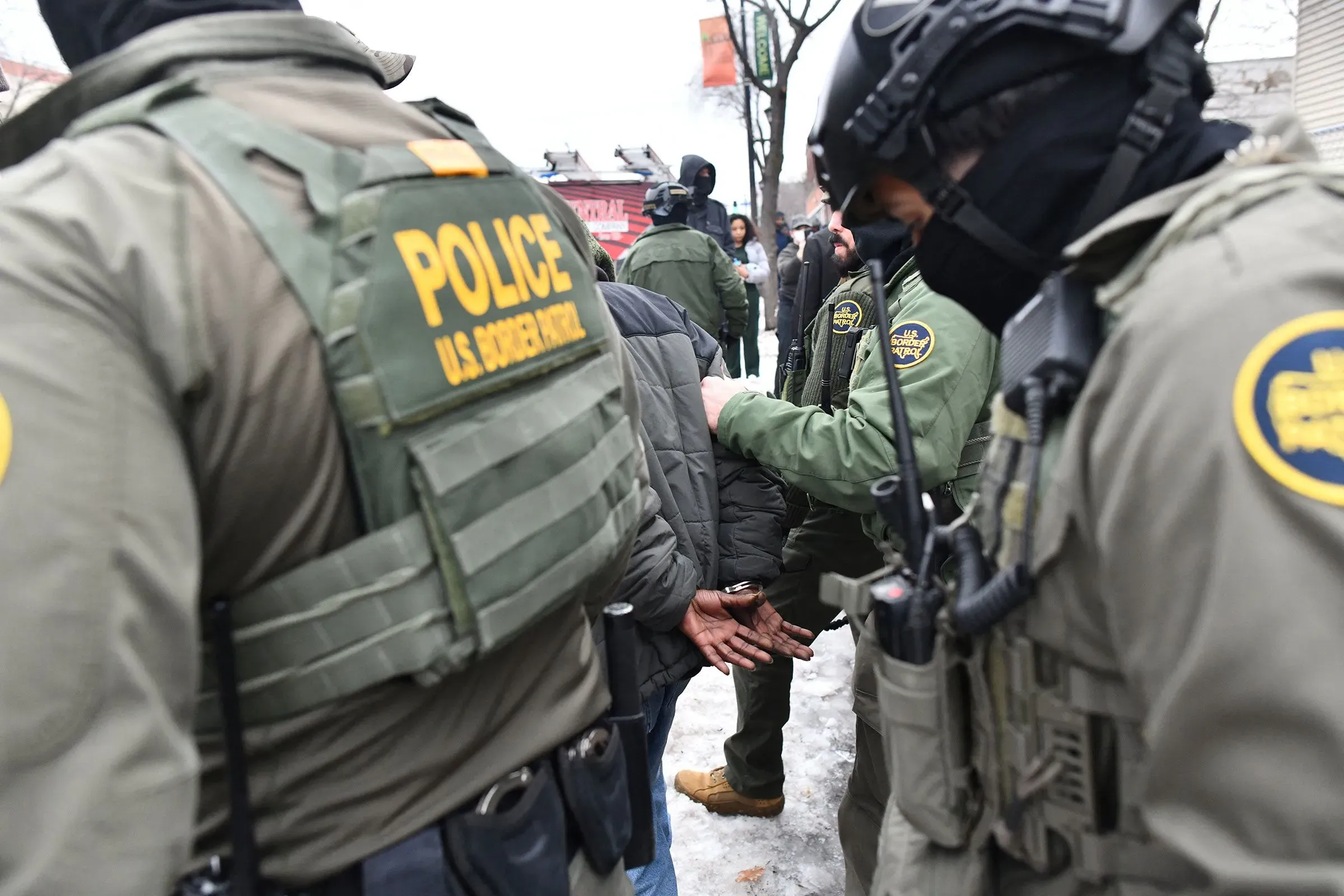 اعتقال شخص من قبل عناصر إنفاذ قوانين الهجرة والجمارك، مع وجود ضباط آخرين في الخلفية، يعكس التوترات بين الولايات الحمراء والزرقاء حول سياسات الهجرة.