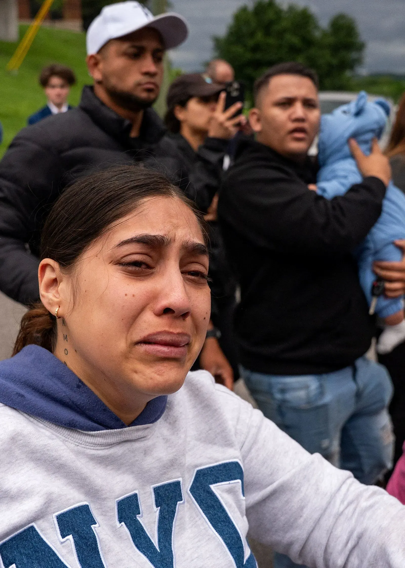 امرأة تبكي في تجمع، تعبر عن مشاعر الحزن والقلق وسط مجموعة من الأشخاص، مما يعكس التوترات حول قضايا الهجرة.