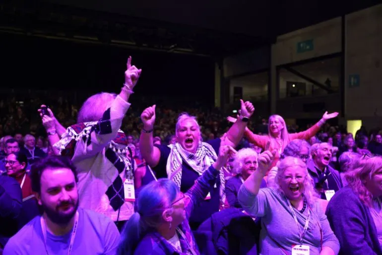 مجموعة من المشاركين في مؤتمر حزب الاشتراكي البريطاني، يعبرون عن حماسهم وأفكارهم بطرق تفاعلية، مع التركيز على الوحدة والتضامن.